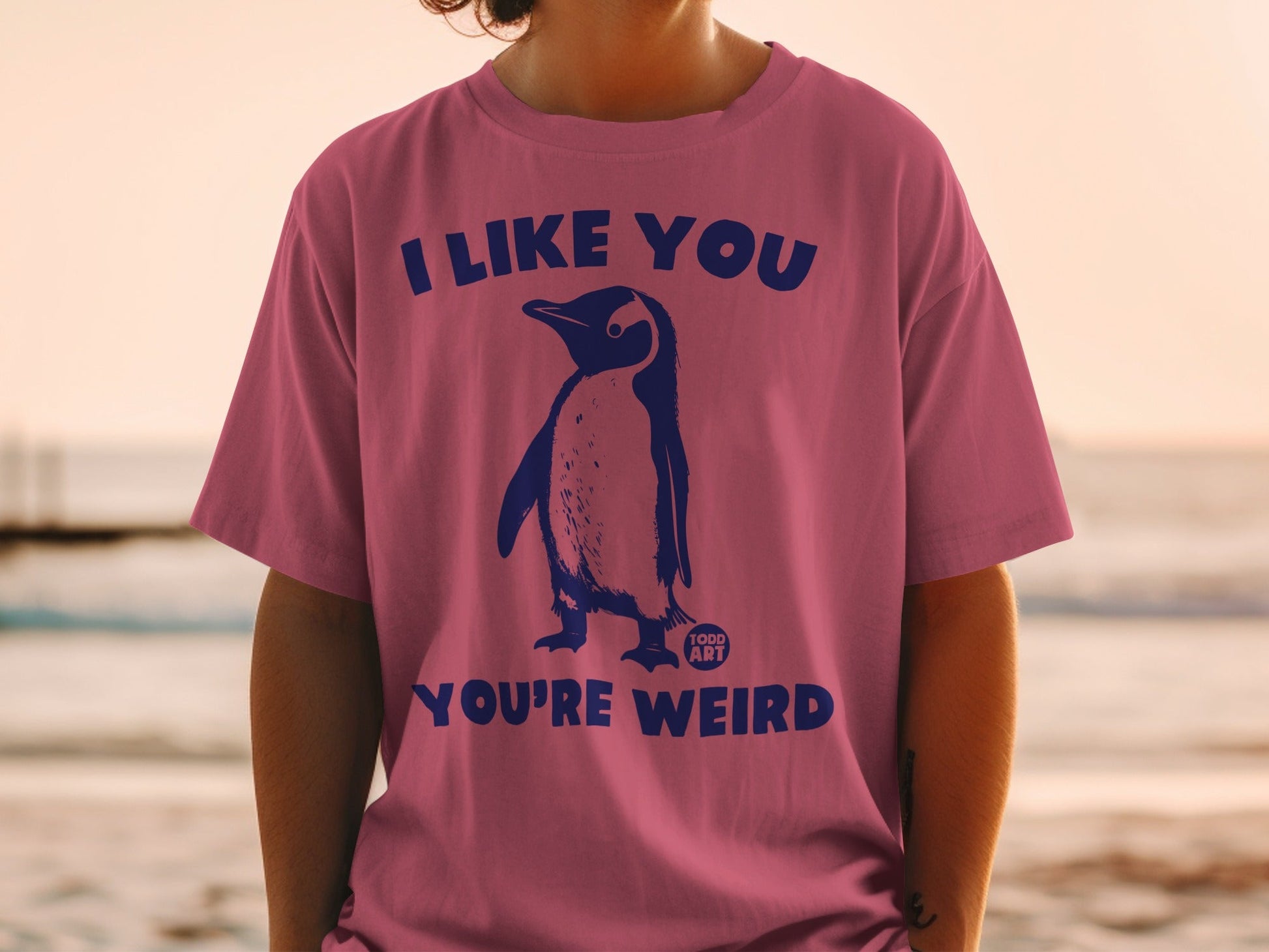 Pink t-shirt with penguin graphic and text "I LIKE YOU YOU'RE WEIRD".
