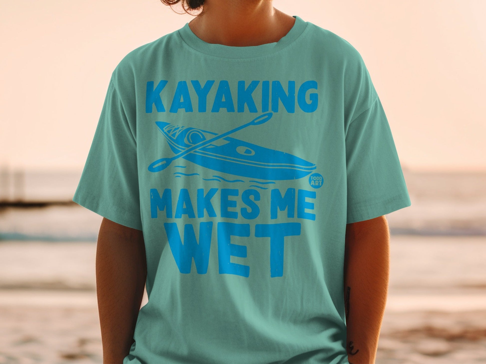 Teal t-shirt with a kayak and paddle graphic and text "Kayaking Makes Me Wet."