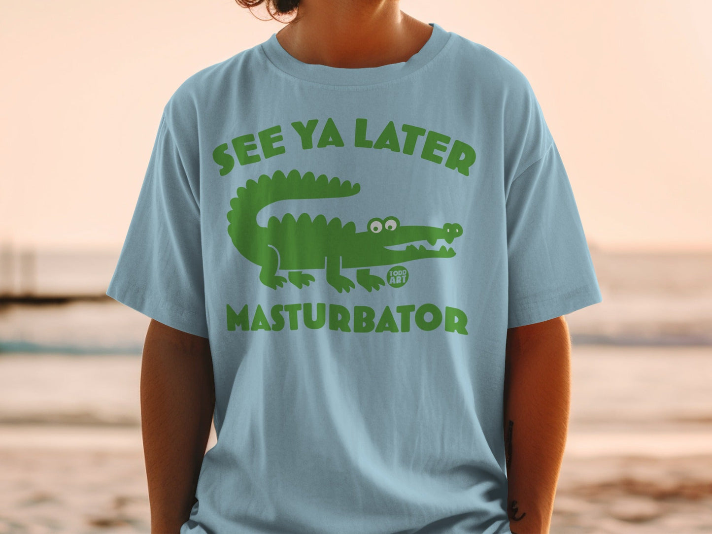Green alligator graphic with "SEE YA LATER MASTURBATOR" text on a light blue t-shirt.