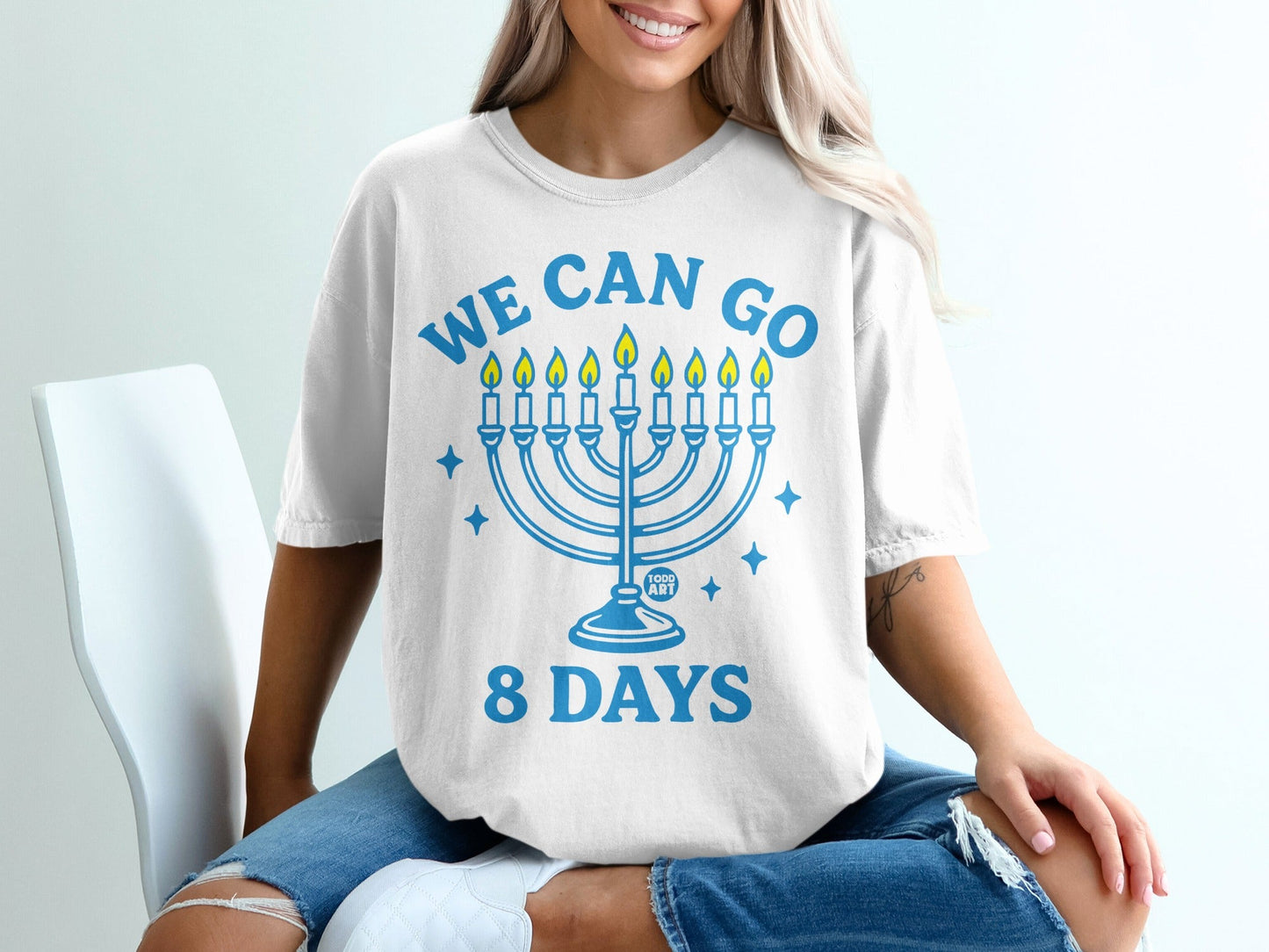 White t-shirt with blue "WE CAN GO 8 DAYS" text and menorah graphic.