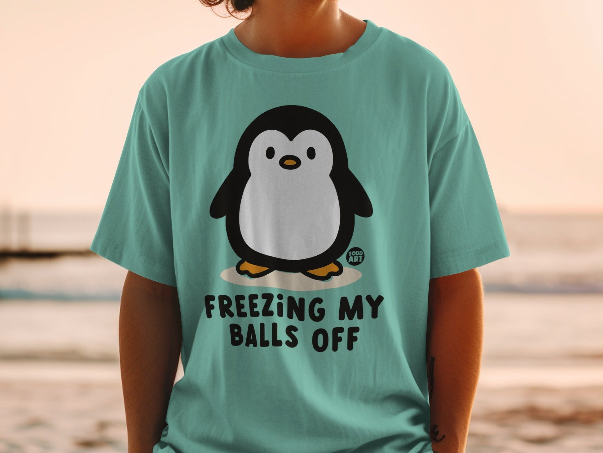 Teal t-shirt with cartoon penguin and text "FREEZING MY BALLS OFF".