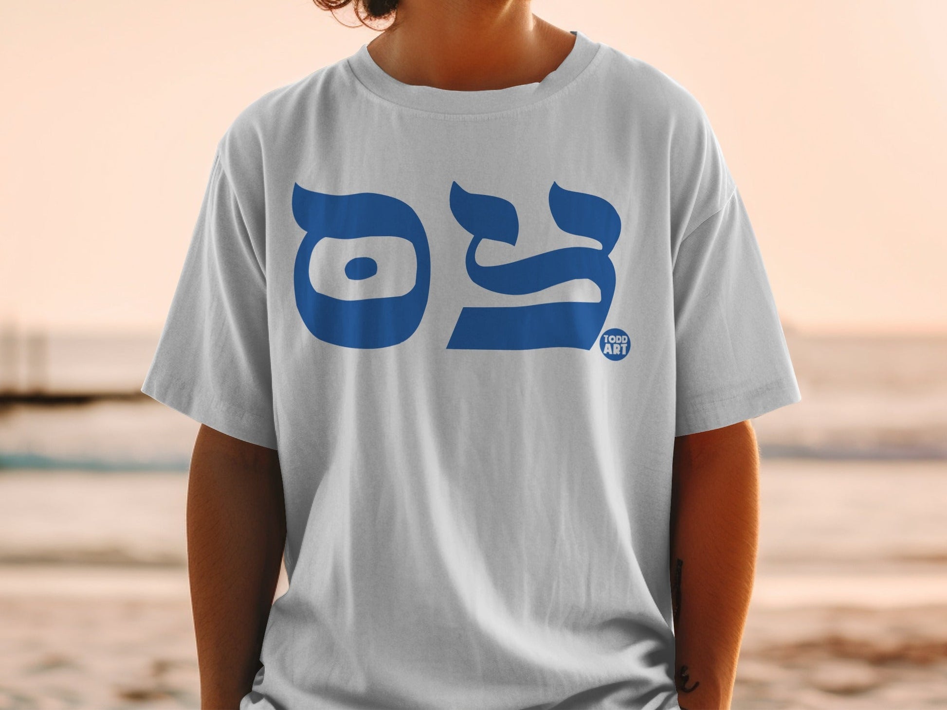 White t-shirt with blue Hebrew text and TODD ART logo on the chest.