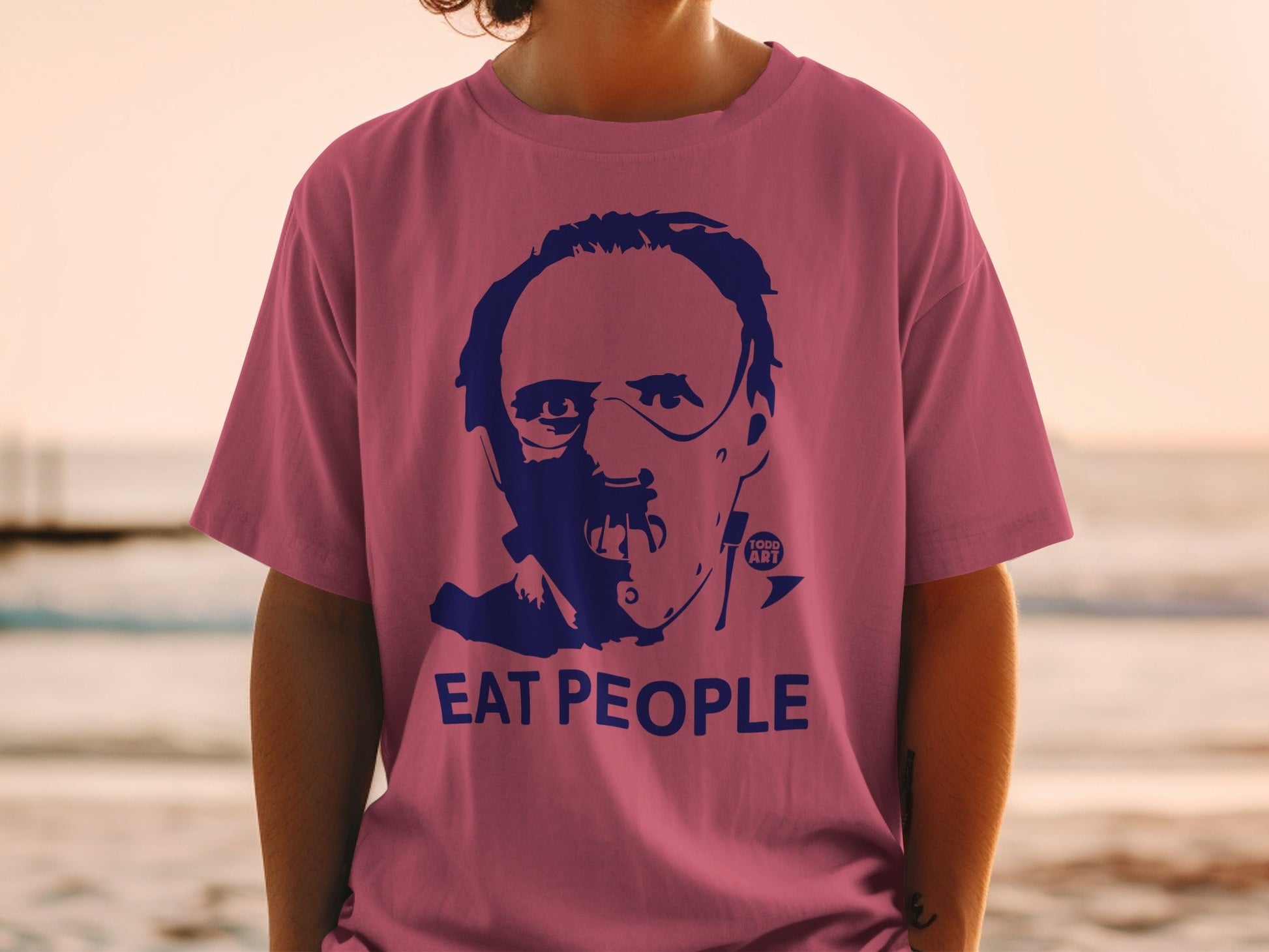 Pink t-shirt with a blue graphic of a man's face and the words "EAT PEOPLE".