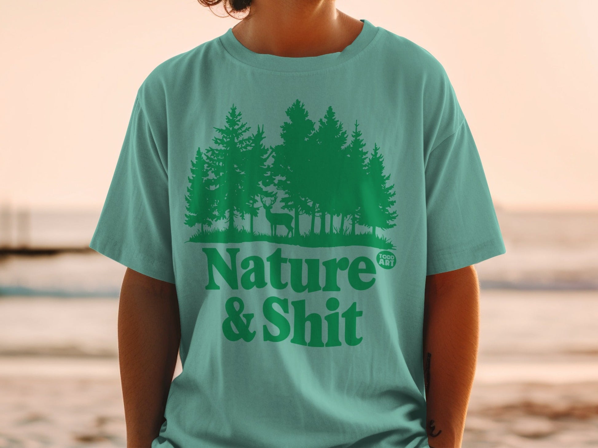 Teal t-shirt with forest, deer, and "Nature & Shit" text graphic.