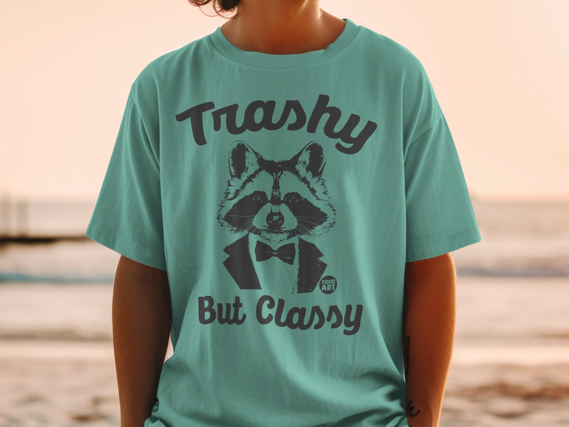 Teal t-shirt with black graphic of raccoon in tuxedo, "Trashy But Classy" text.