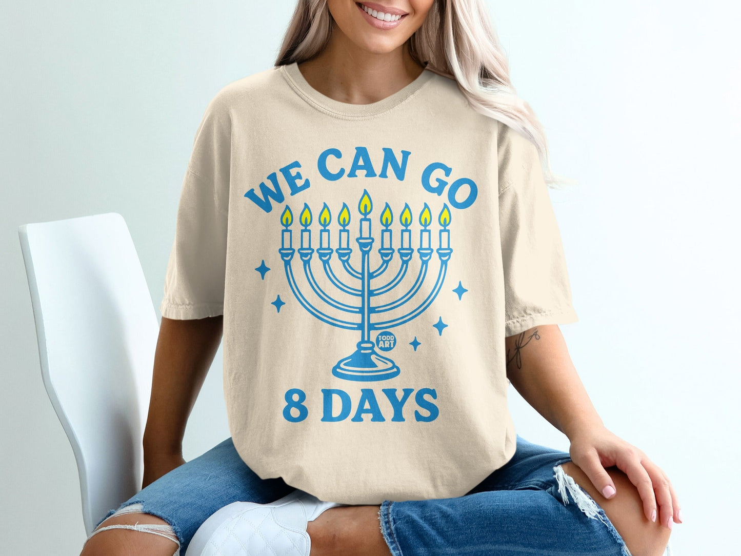 Cream t-shirt with blue text "WE CAN GO 8 DAYS" and a menorah graphic.