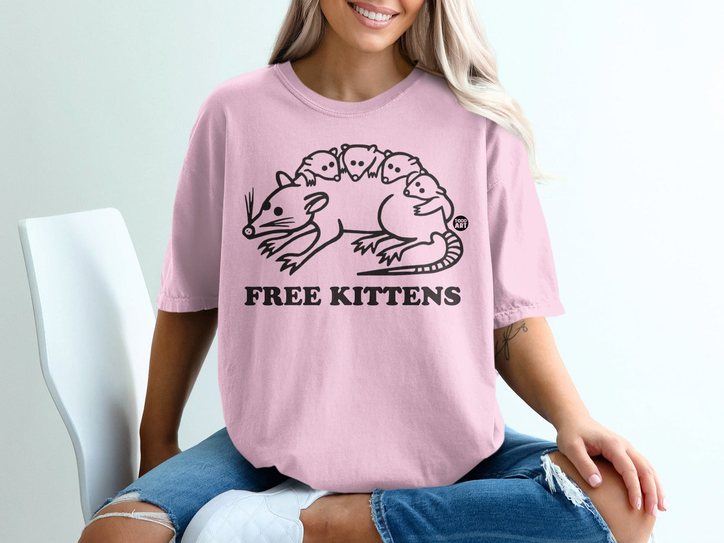 Pink t-shirt with a stylized drawing of a rat carrying kittens and text "FREE KITTENS".