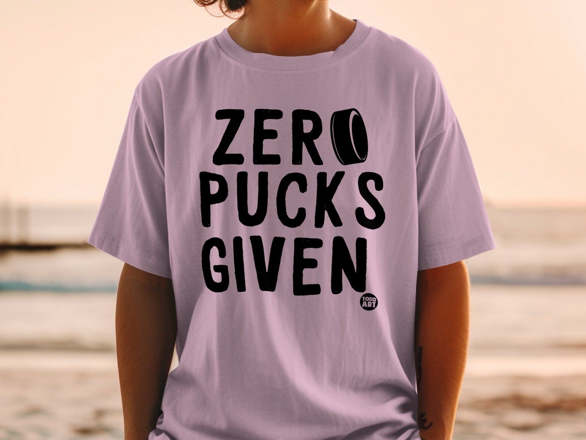 Lavender t-shirt with "ZERO PUCKS GIVEN" text and hockey puck graphic.