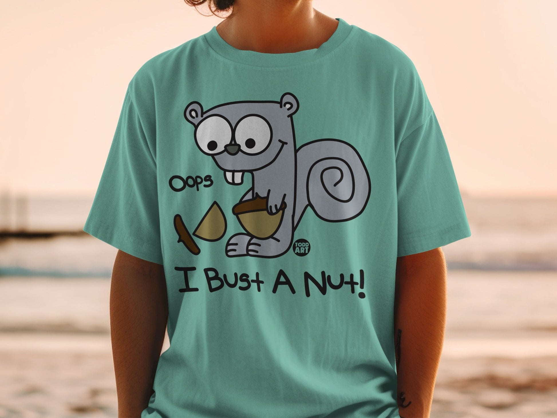 Teal t-shirt with a cartoon squirrel holding a nut, "Oops, I Bust a Nut!" text.