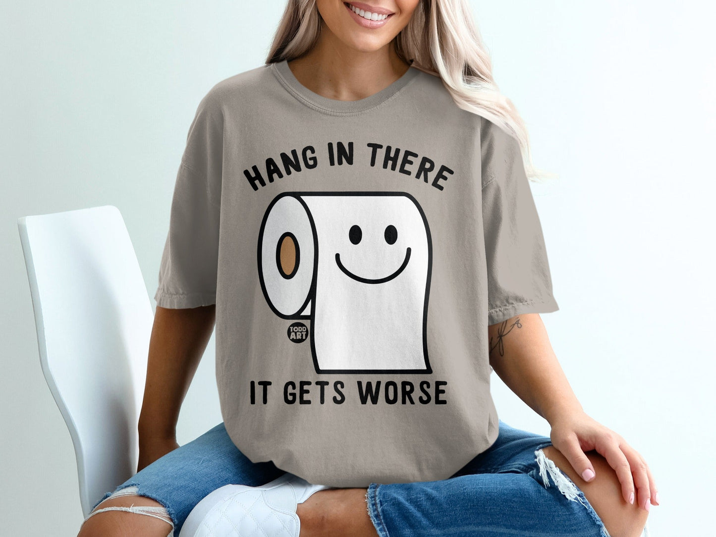 T-shirt with cartoon toilet paper roll and text "HANG IN THERE IT GETS WORSE".