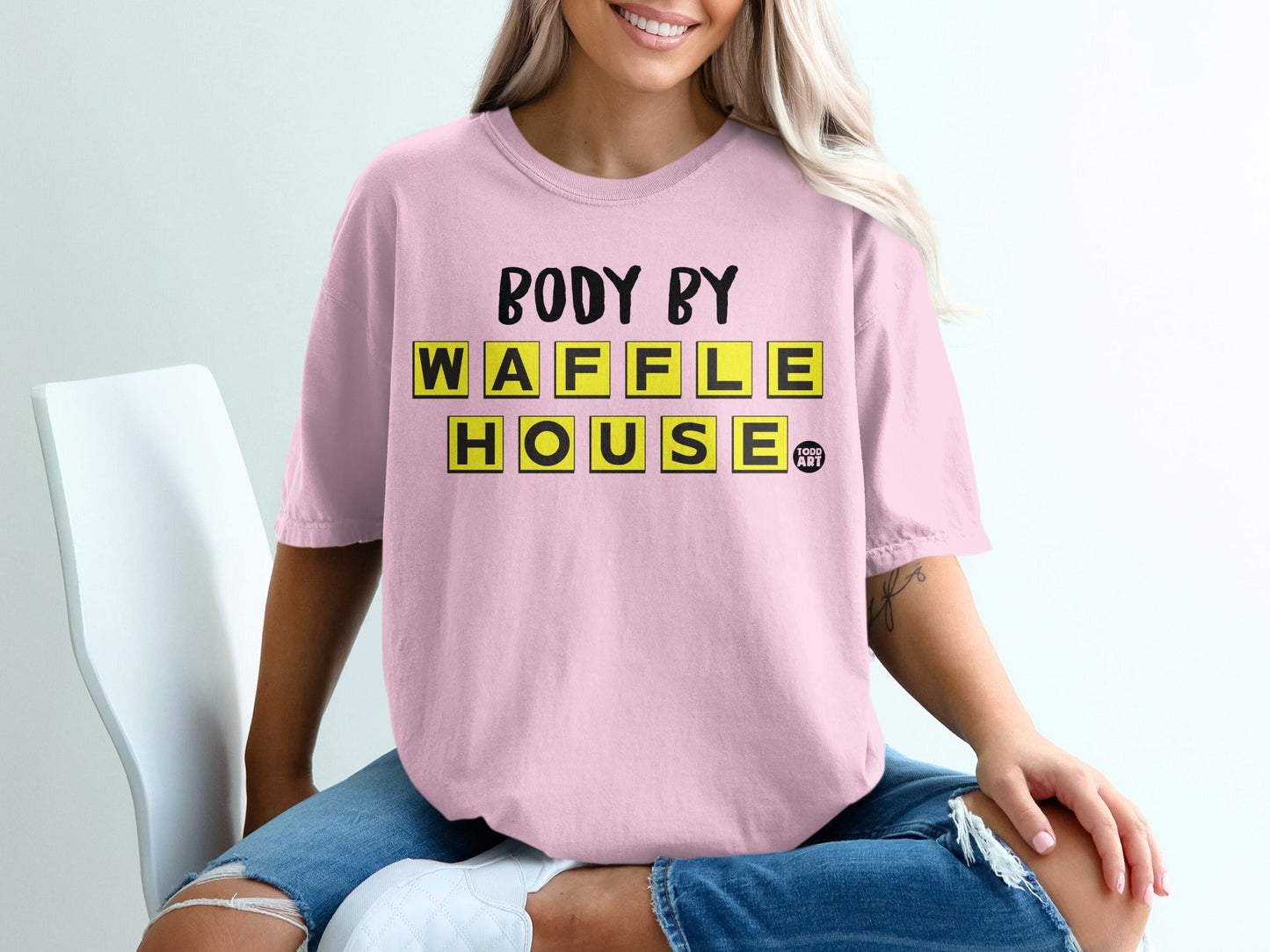 Pink t-shirt with "Body by Waffle House" in yellow tile letters.