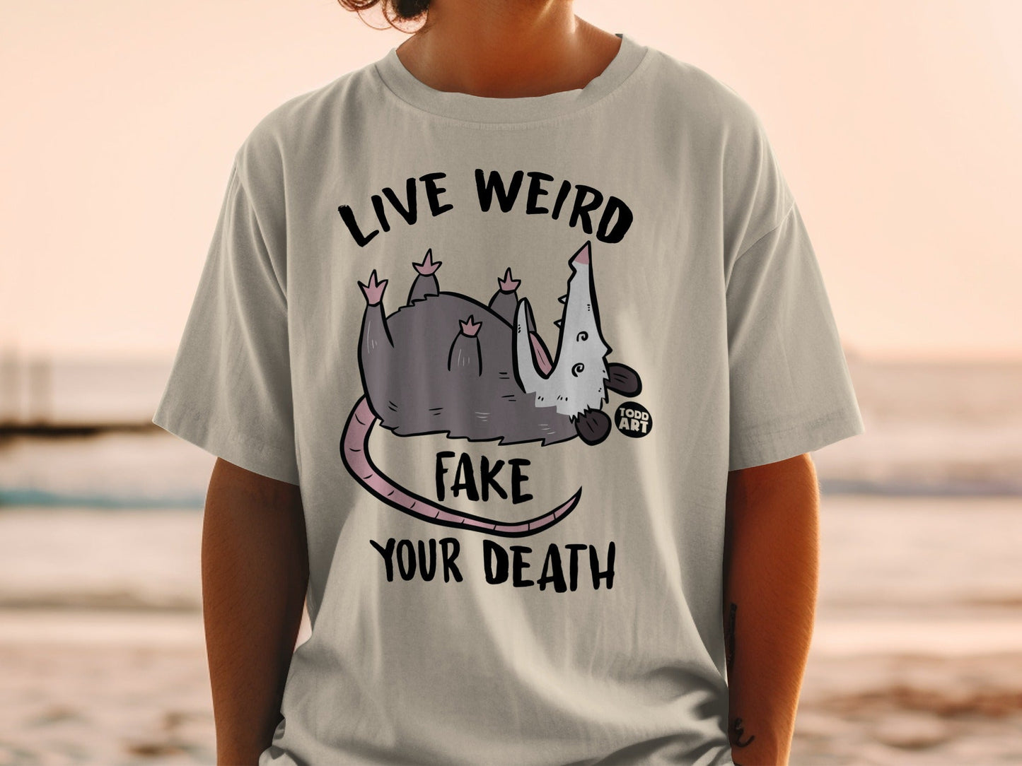 T-shirt with opossum and text "LIVE WEIRD FAKE YOUR DEATH".