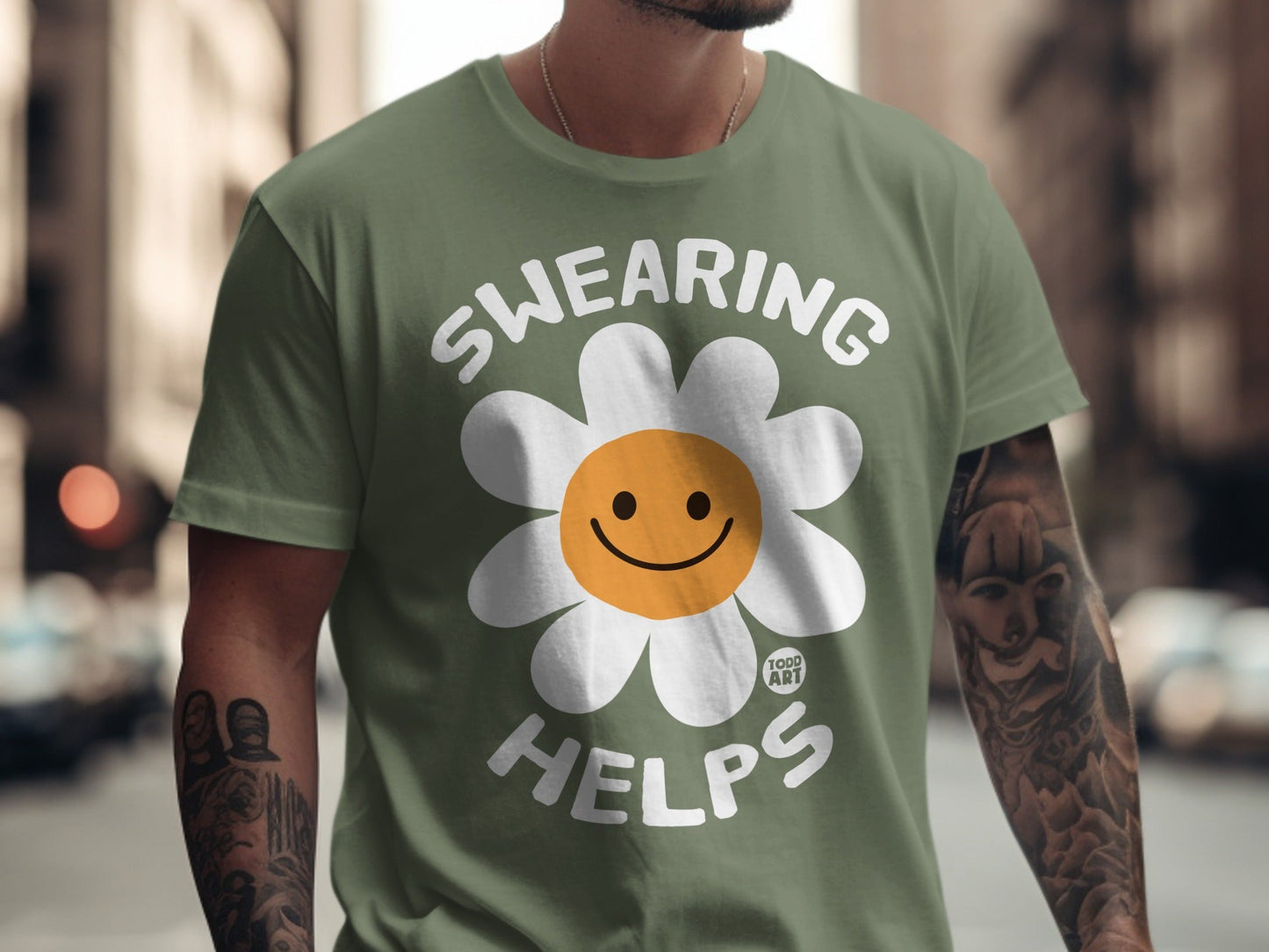 Green t-shirt with a white daisy graphic and "SWEARING HELPS" text.