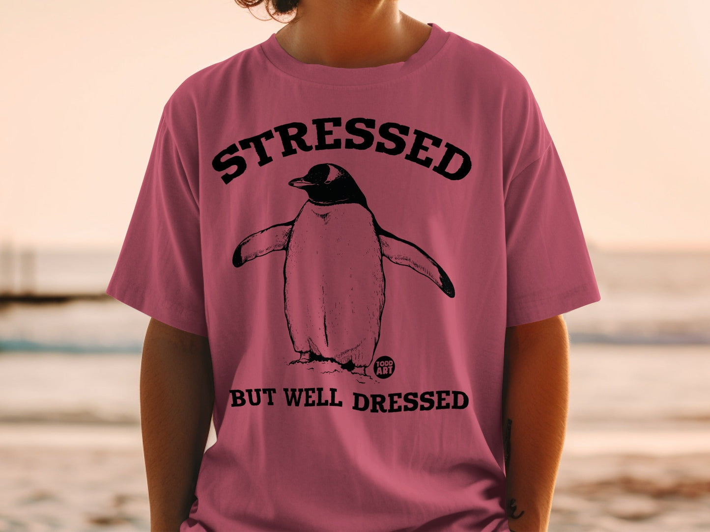Pink t-shirt with a penguin illustration and text "STRESSED BUT WELL DRESSED".