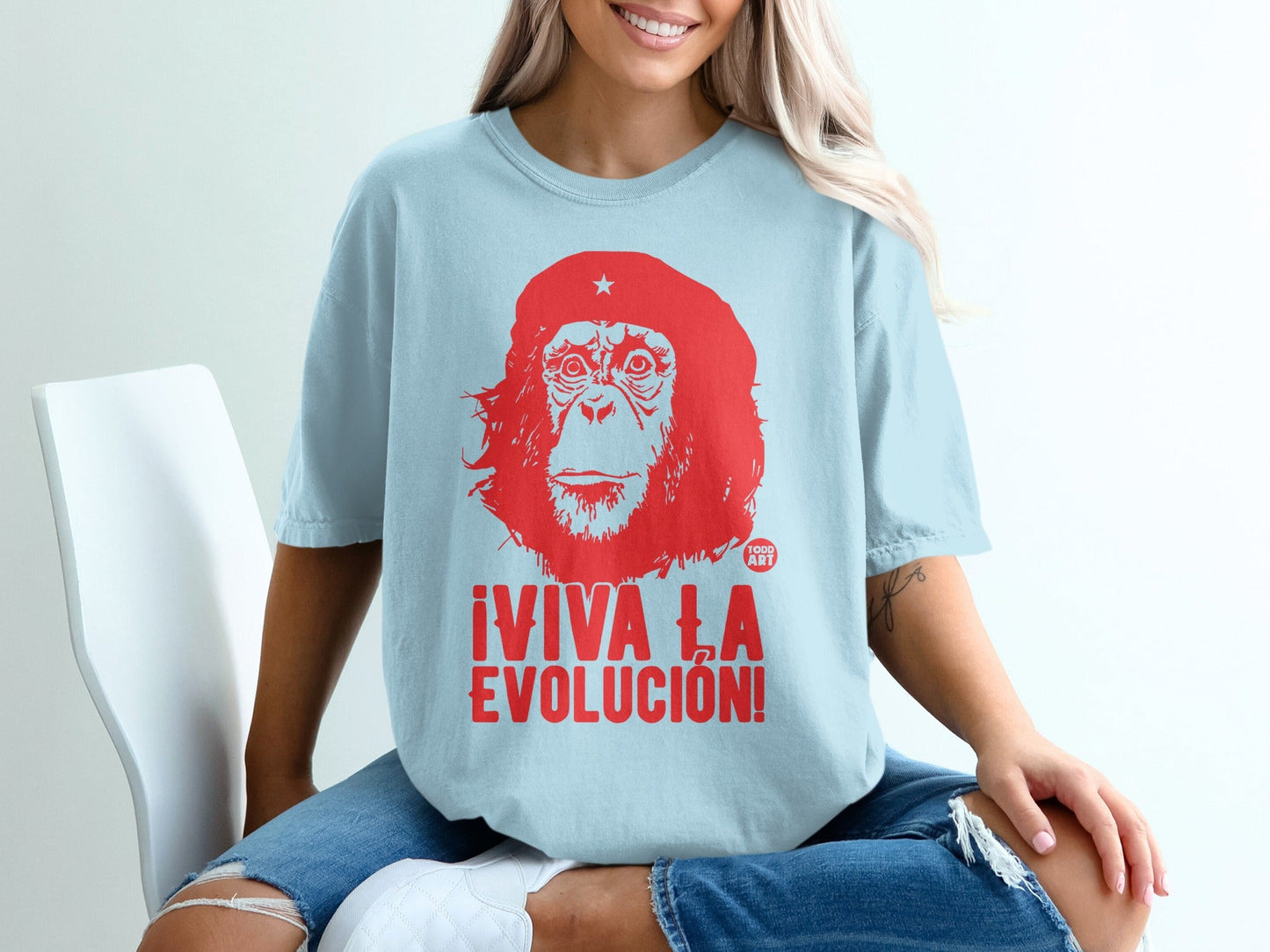 Light blue t-shirt with a red graphic of a primate head and "¬°VIVA LA EVOLUCI√ìN!" text.