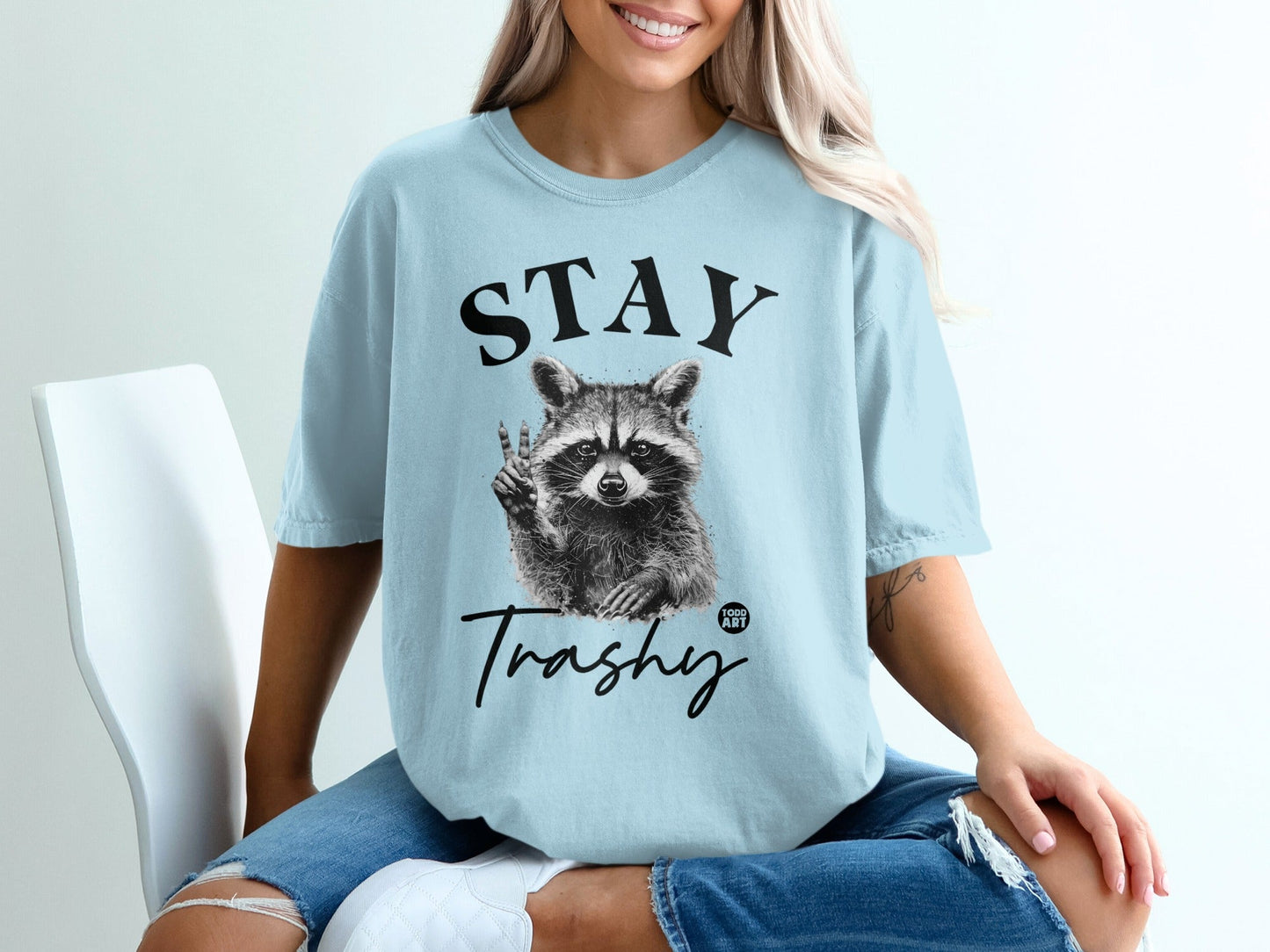 Light blue t-shirt with raccoon graphic and "STAY Trashy" text.