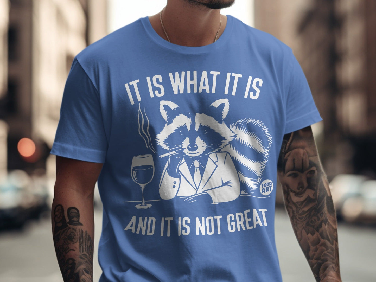 Blue t-shirt with raccoon in suit, smoking and holding wine glass. Text reads "It is what it is and it is not great."