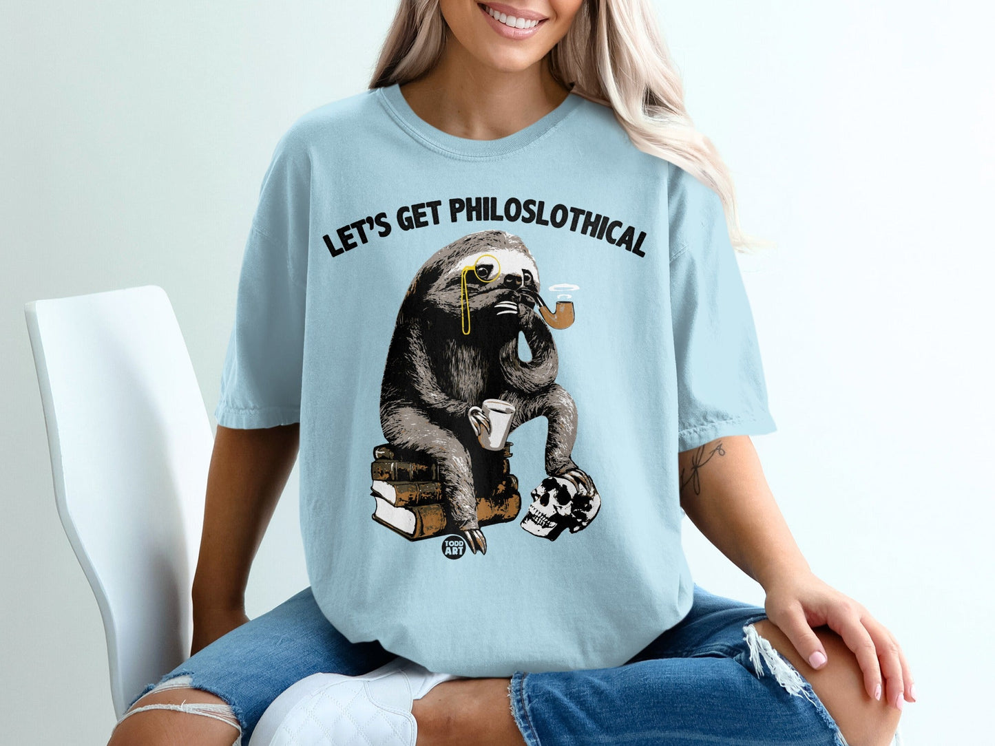 Light blue t-shirt with sloth on books, pipe, skull, and text "LET'S GET PHILOSLOTHICAL".