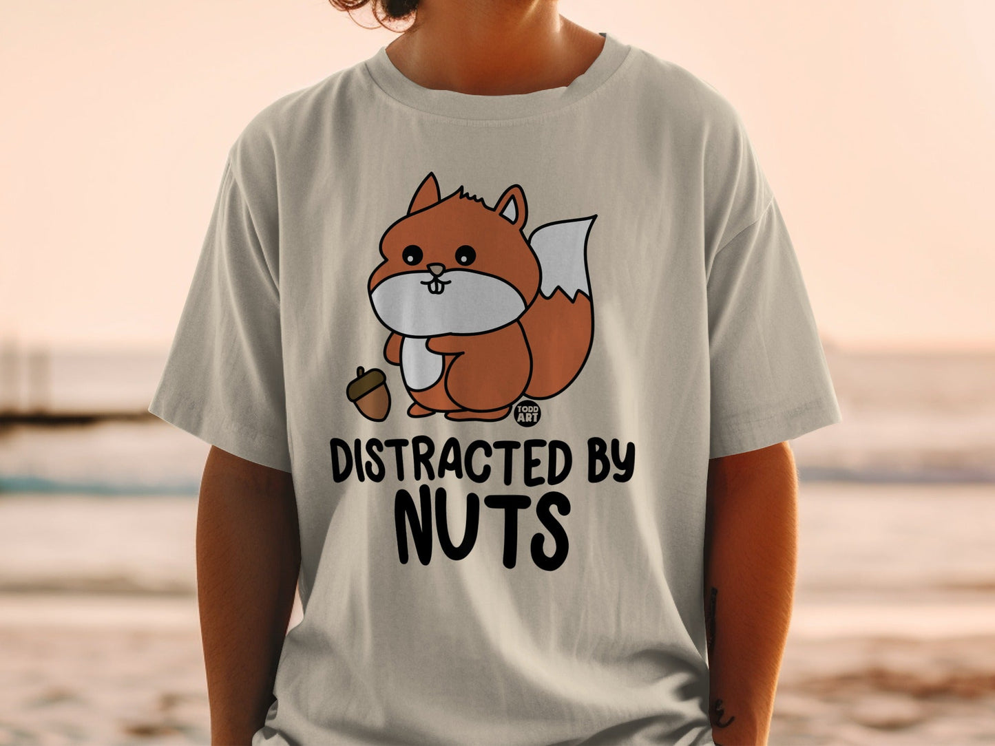 Cartoon squirrel holding acorn on t-shirt with text "DISTRACTED BY NUTS".