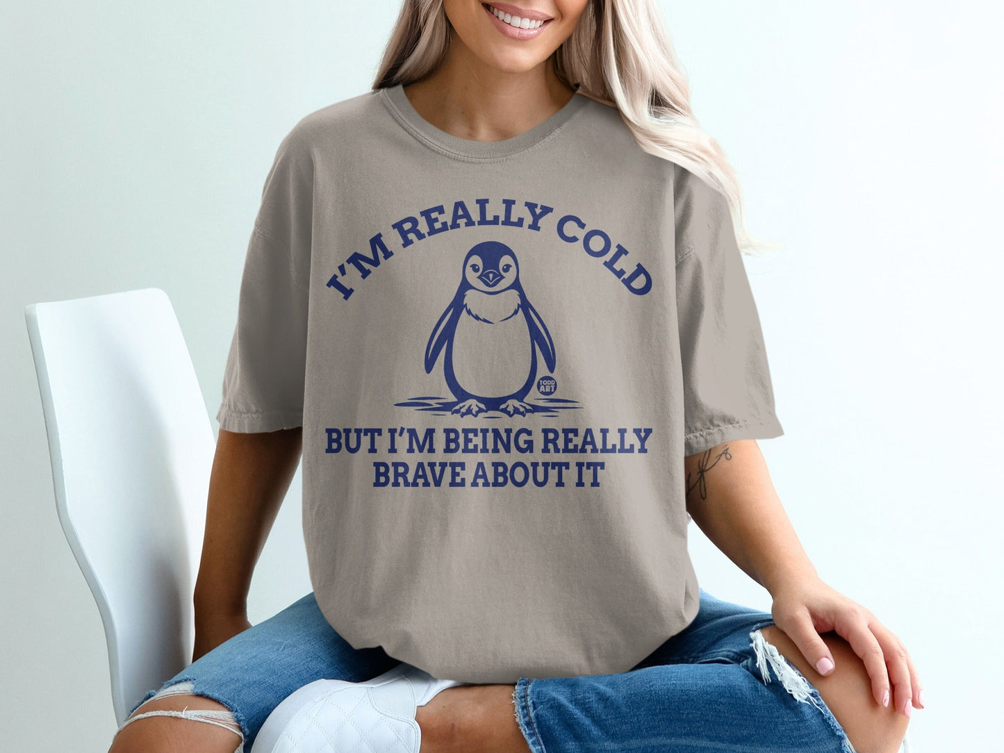 Woman wearing a tan t-shirt with a penguin and text "I'M REALLY COLD BUT I'M BEING REALLY BRAVE ABOUT IT".