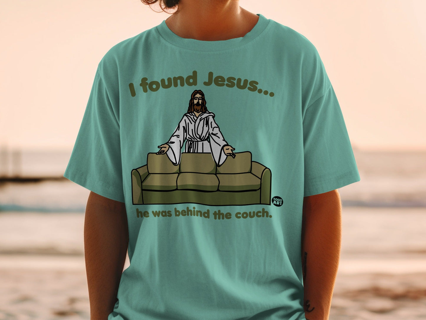 T-shirt with "I found Jesus... he was behind the couch" text and cartoon image.