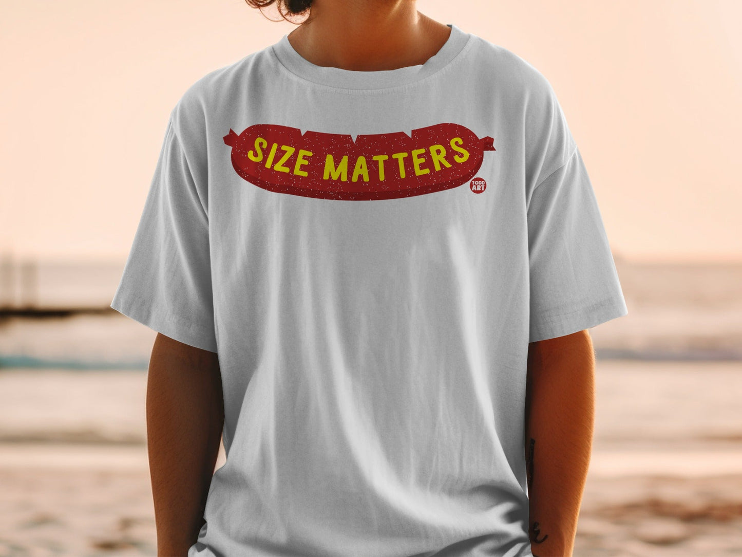 White t-shirt with "SIZE MATTERS" printed in bold yellow letters on a sausage graphic.