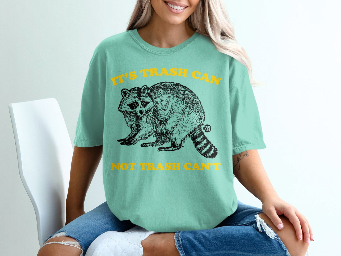 Teal t-shirt with raccoon graphic and text "IT'S TRASH CAN NOT TRASH CAN'T".