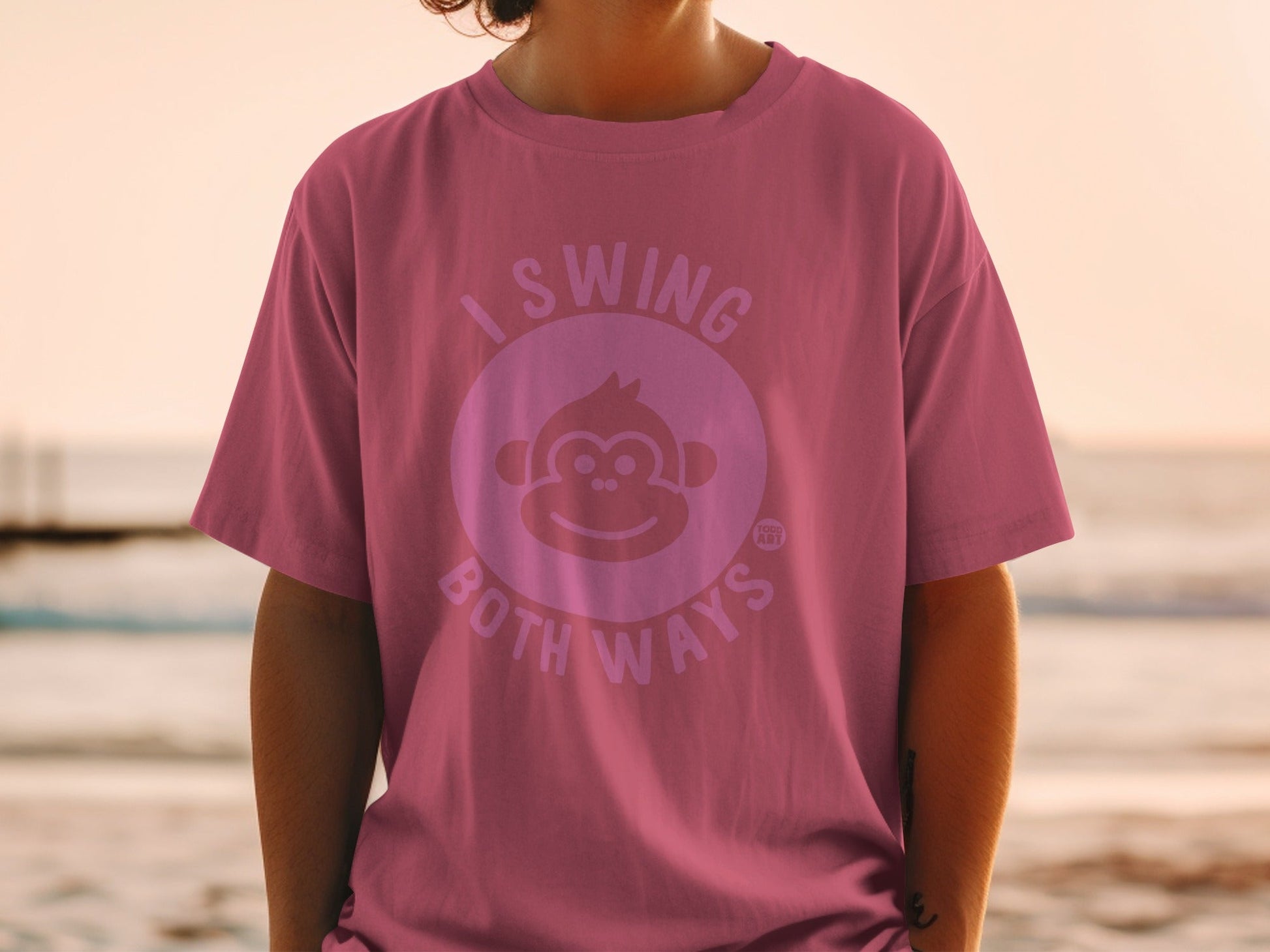 Pink t-shirt with a smiling monkey graphic and text "I SWING BOTH WAYS".