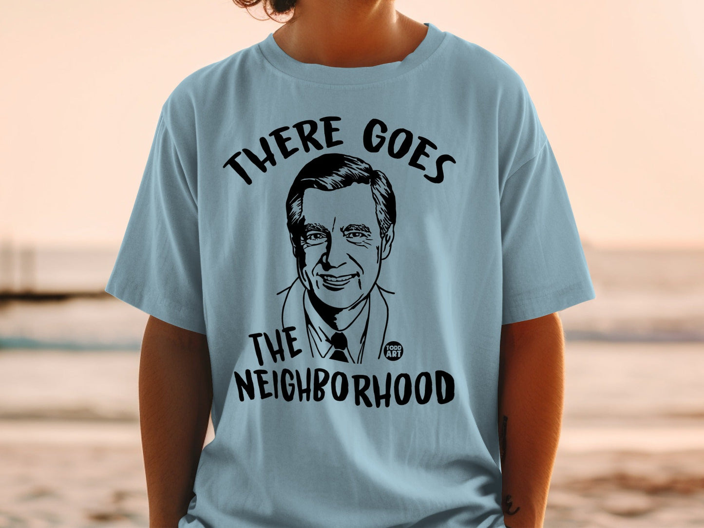 Light blue t-shirt with a black graphic of Fred Rogers and text "THERE GOES THE NEIGHBORHOOD".