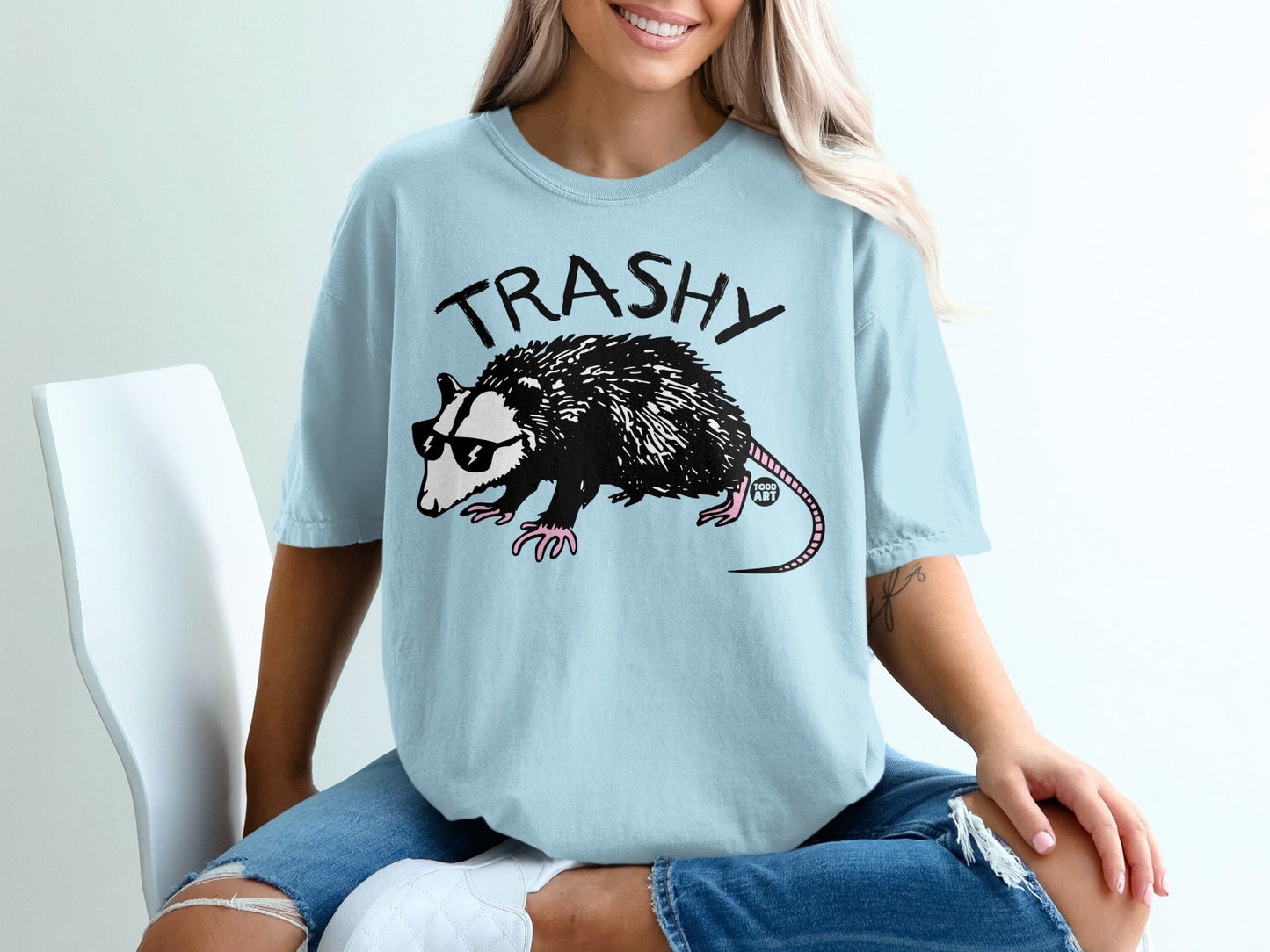 Light blue t-shirt with "TRASHY" text and a cool opossum graphic.