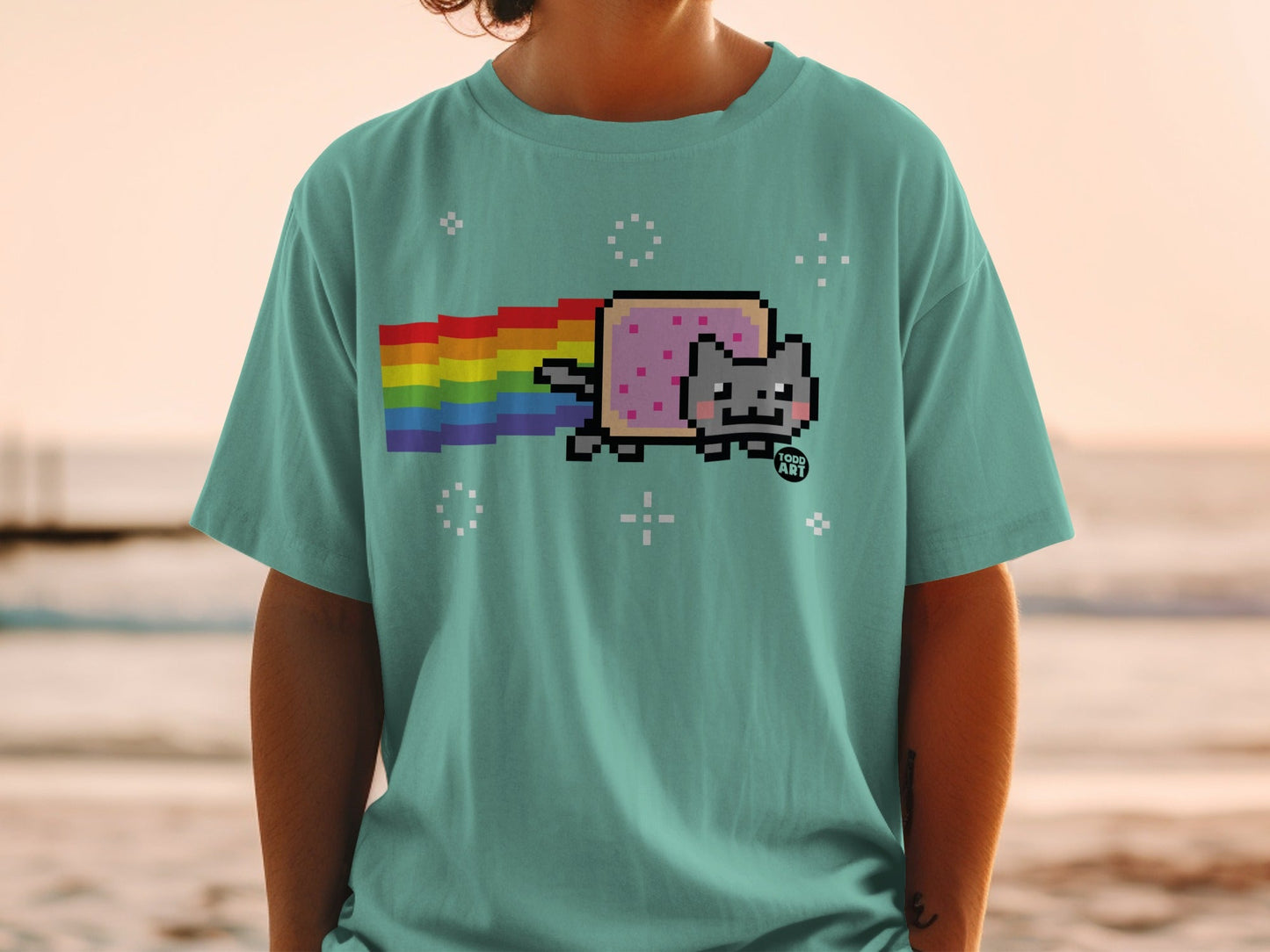 Pixelated cat with rainbow trail on teal t-shirt.