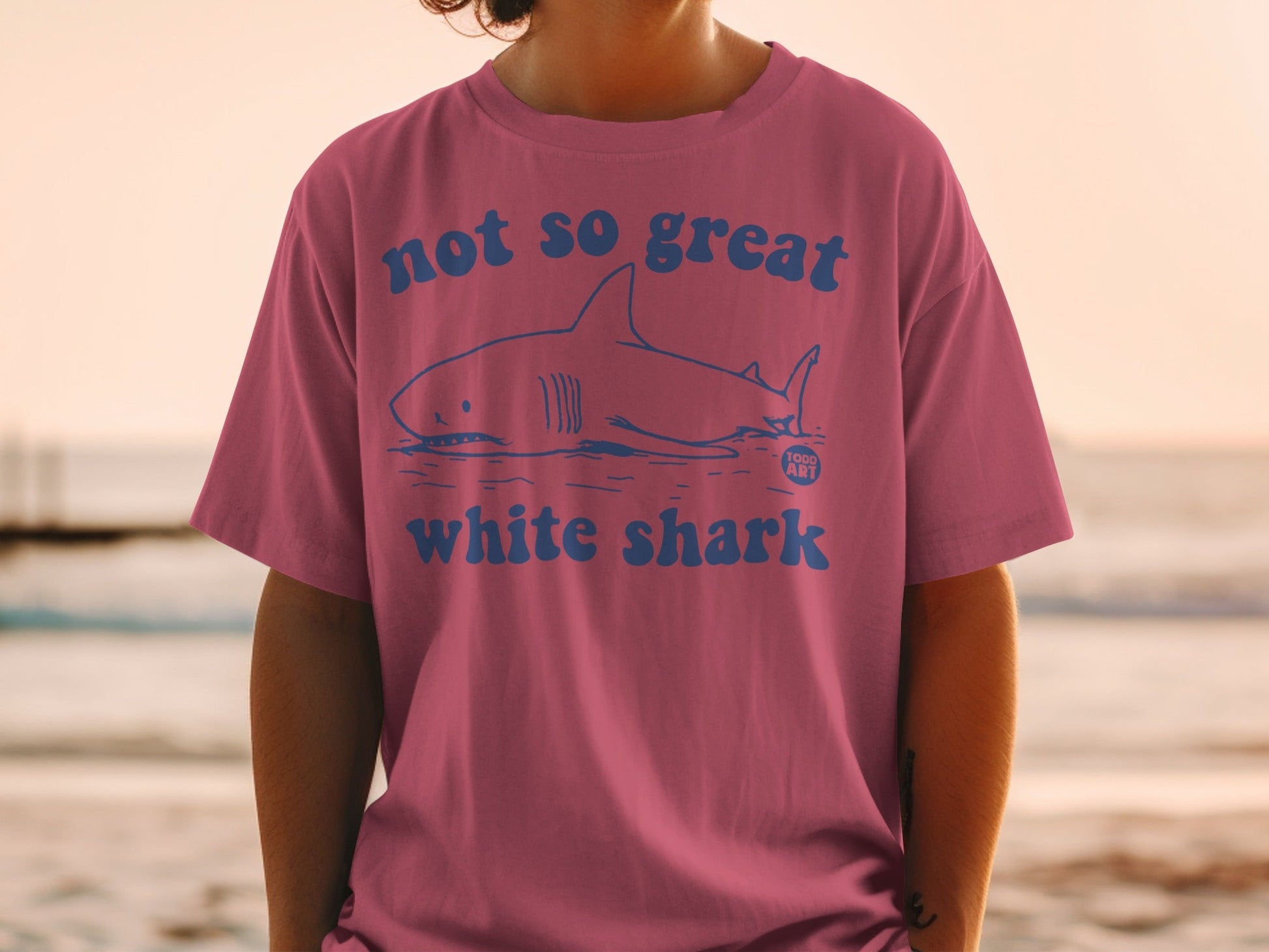 Pink t-shirt with blue text and a graphic of a great white shark.