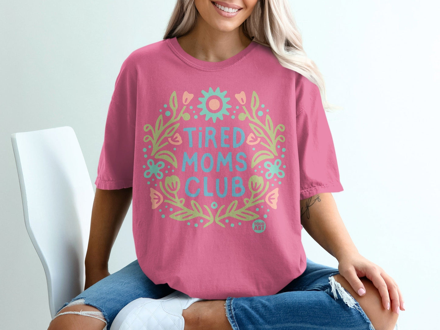 Pink t-shirt with "Tired Moms Club" in a floral wreath graphic.