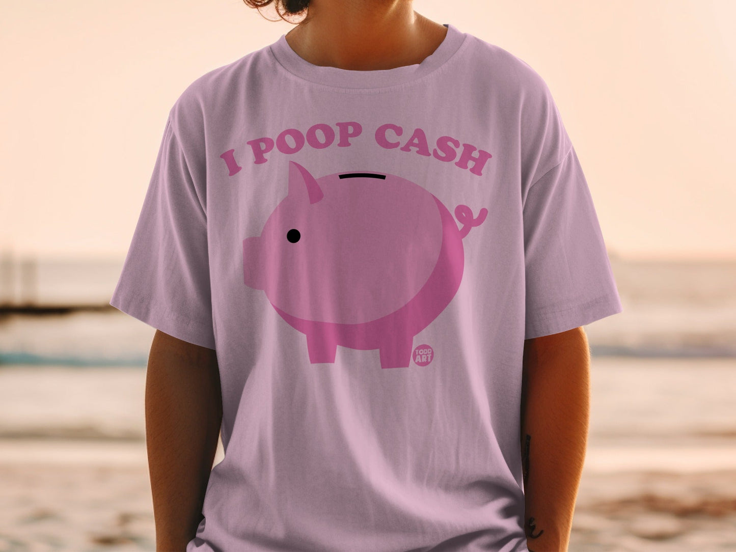 Pink piggy bank graphic with text "I POOP CASH" on a light purple t-shirt.