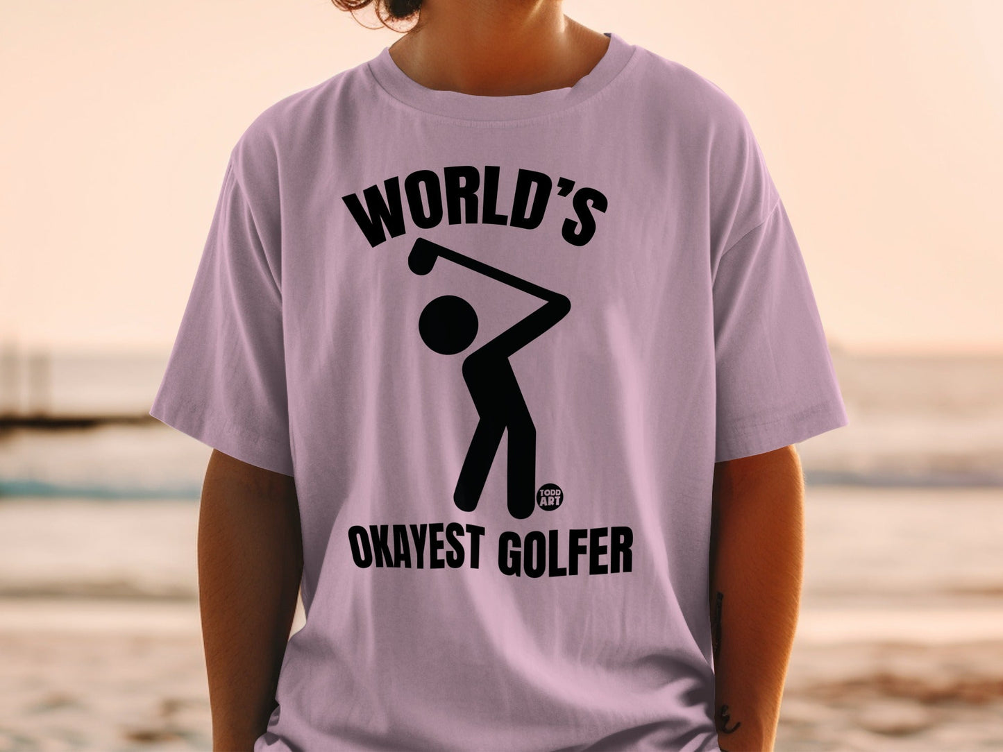 Black graphic of a golfer with "WORLD'S OKAYEST GOLFER" text on a lilac t-shirt.