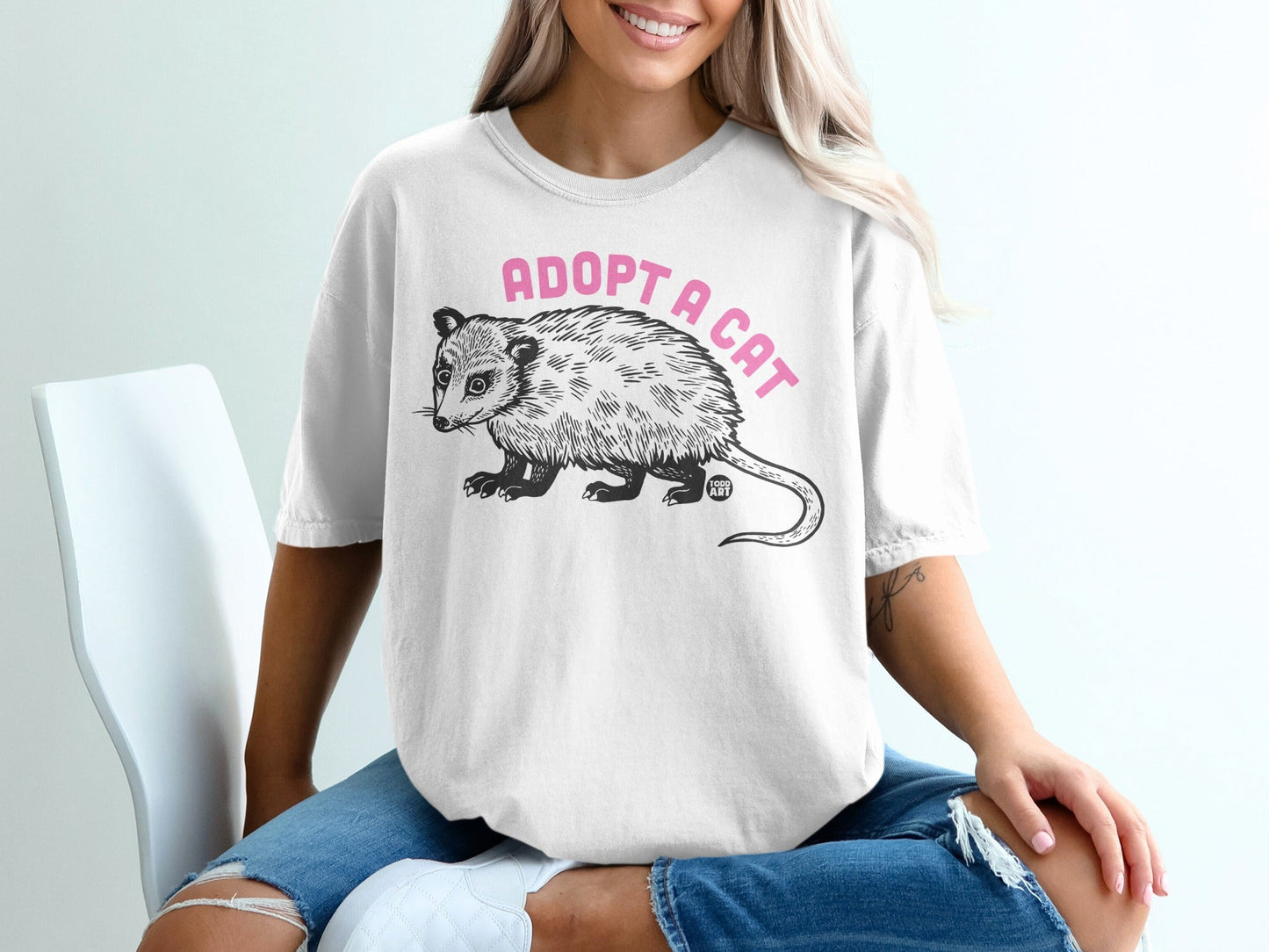 White t-shirt with "Adopt a Cat" and an opossum graphic.