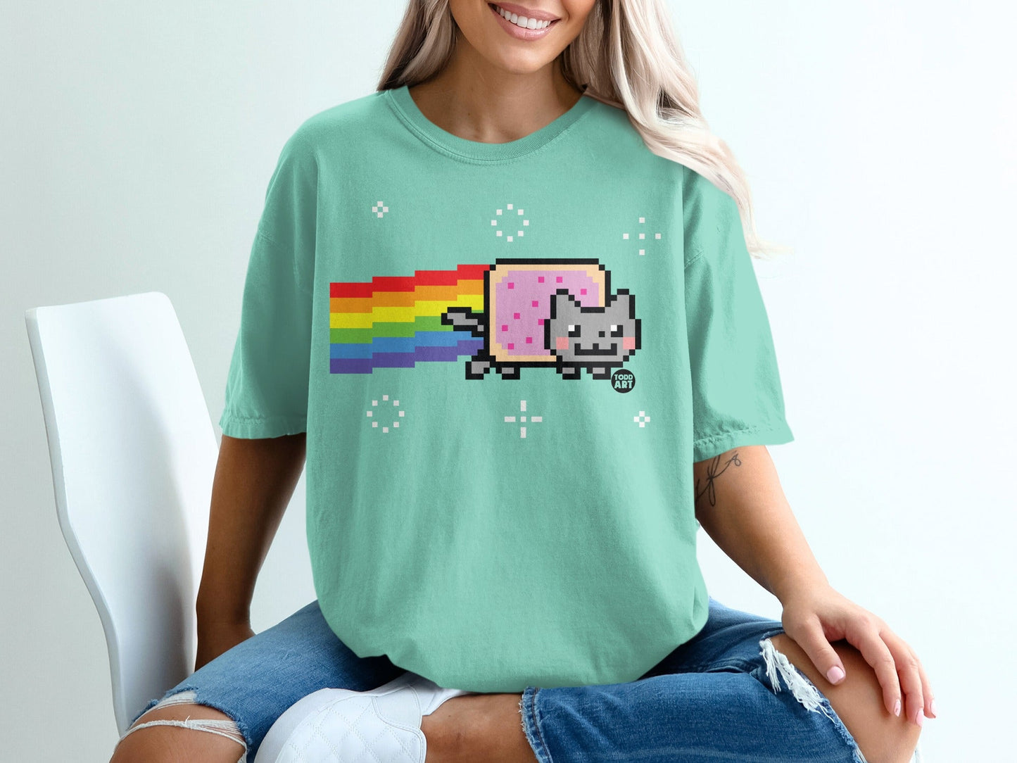 Pixelated cat with rainbow tail on a mint green t-shirt.