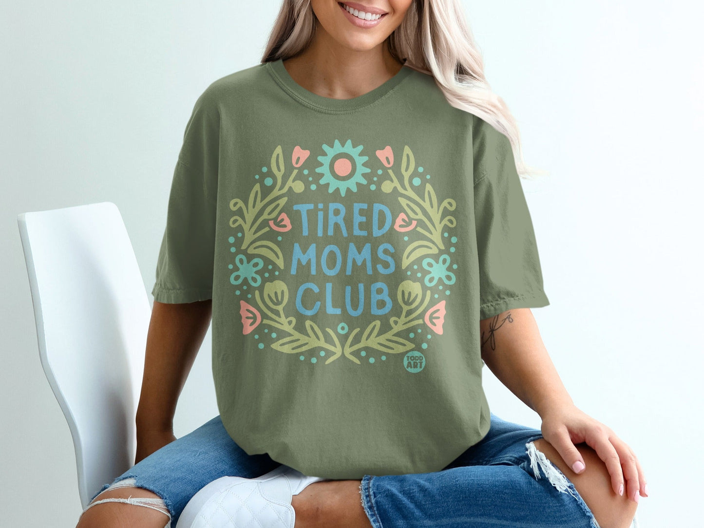 Green t-shirt with "Tired Moms Club" in floral wreath graphic.