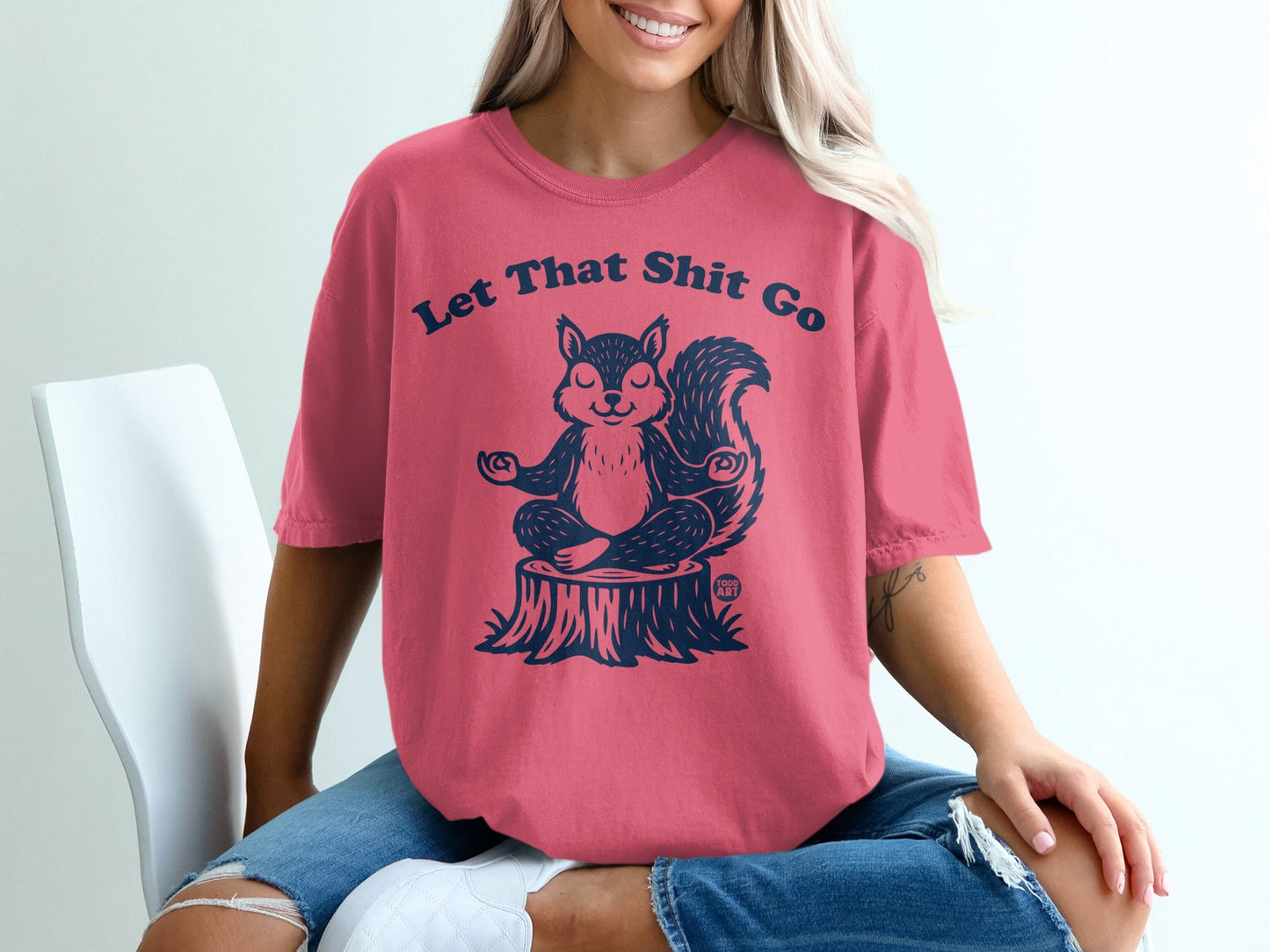 Coral t-shirt with "Let That Shit Go" text and meditating squirrel graphic.