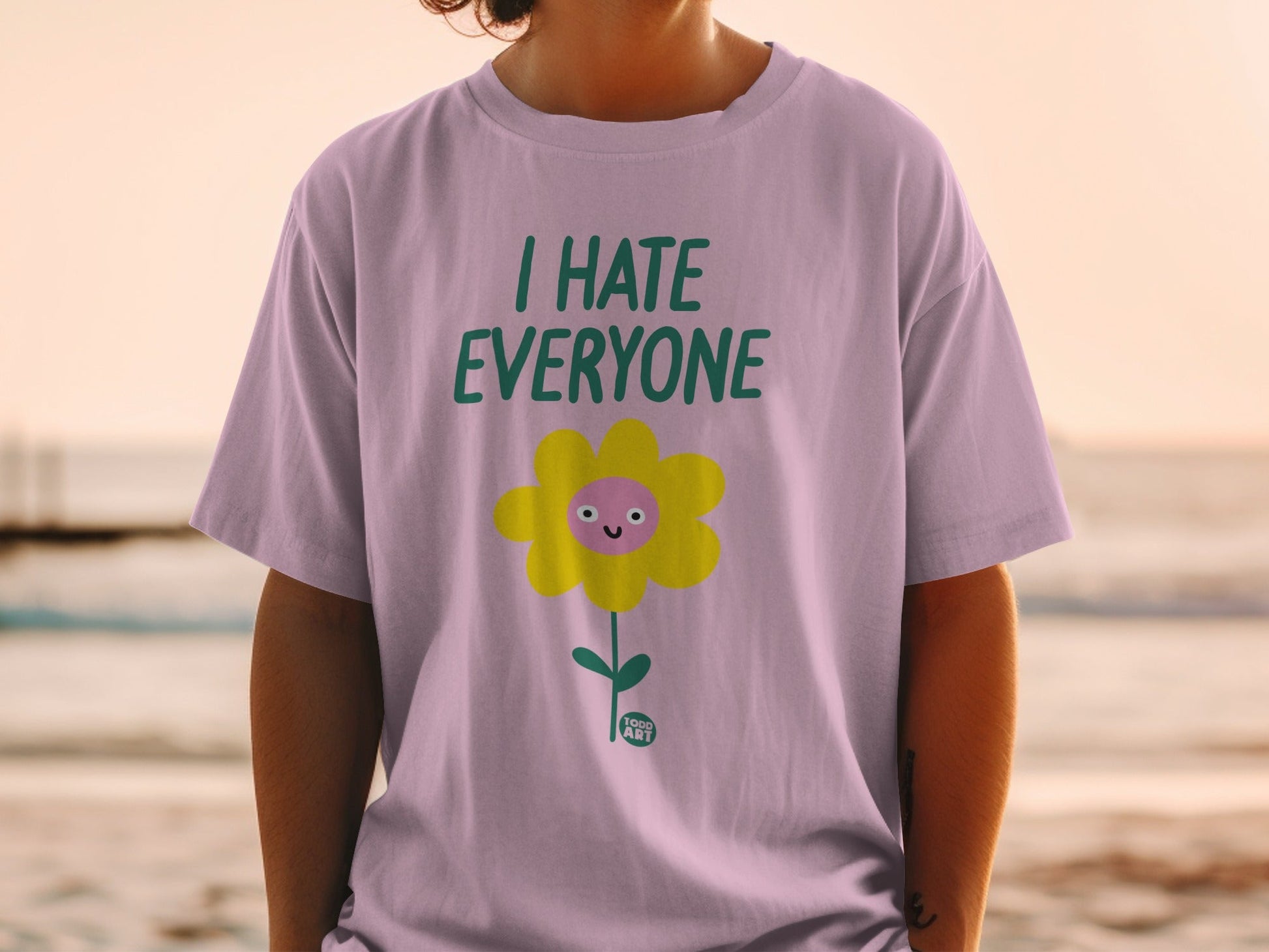 Lilac t-shirt with cartoon yellow flower and text "I HATE EVERYONE".