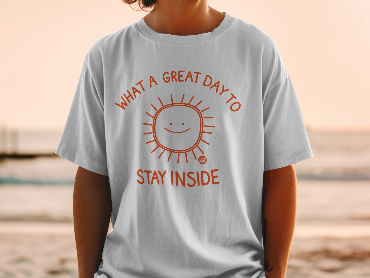 White t-shirt with orange sun graphic and text "WHAT A GREAT DAY TO STAY INSIDE".