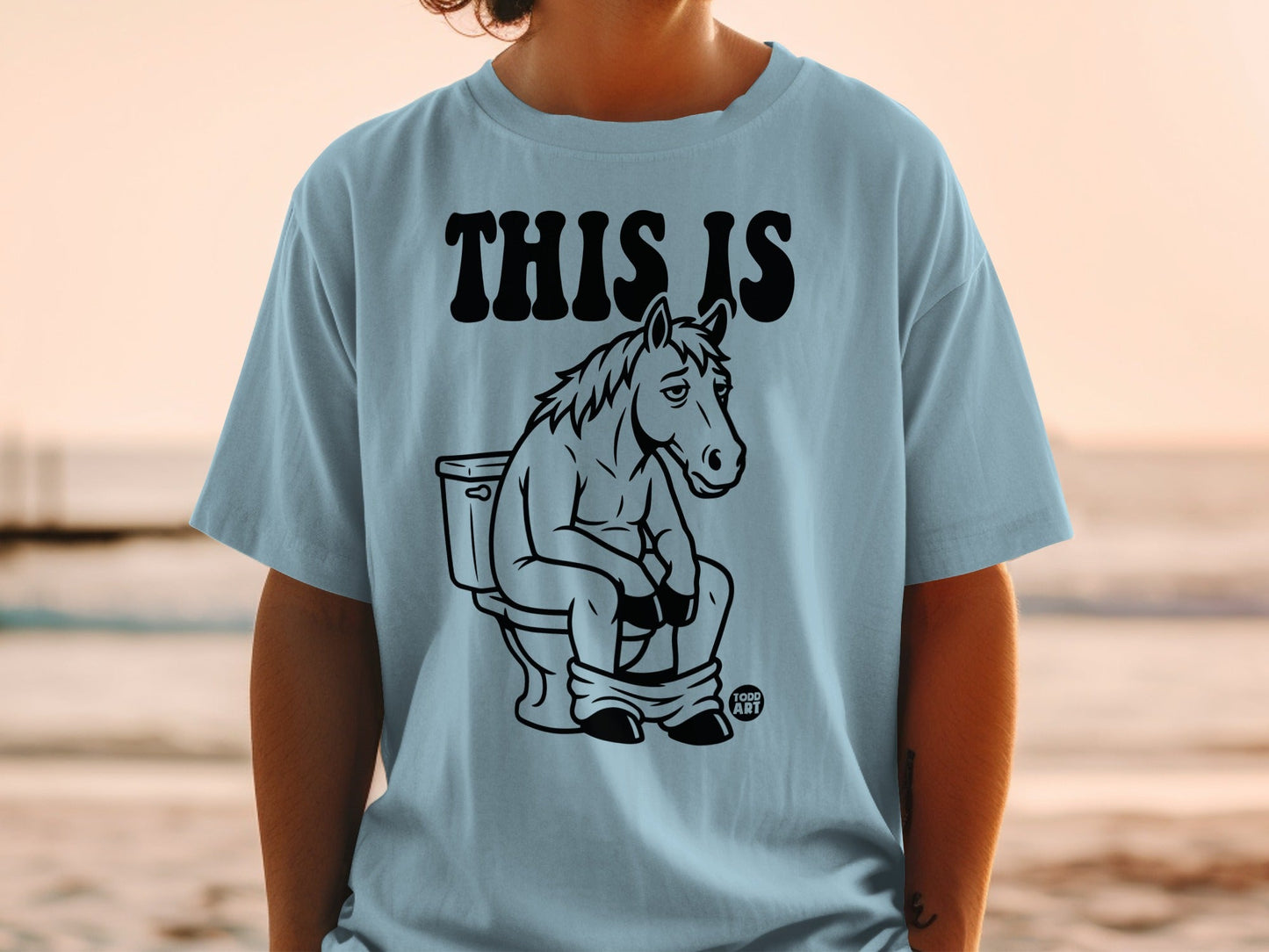 Light blue t-shirt with black graphic of a horse sitting on a toilet.