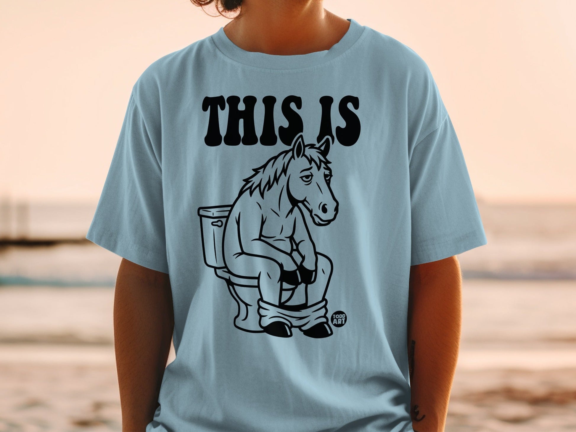 Light blue t-shirt with black graphic of a horse sitting on a toilet.
