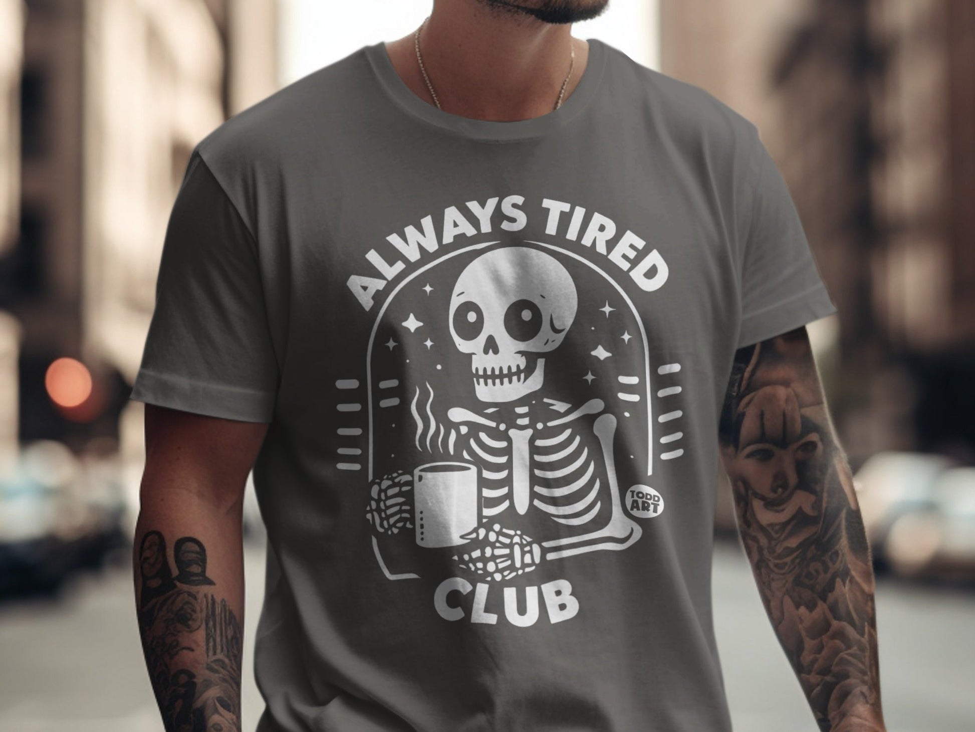 Gray t-shirt with white skeleton holding coffee mug and "ALWAYS TIRED CLUB" text.