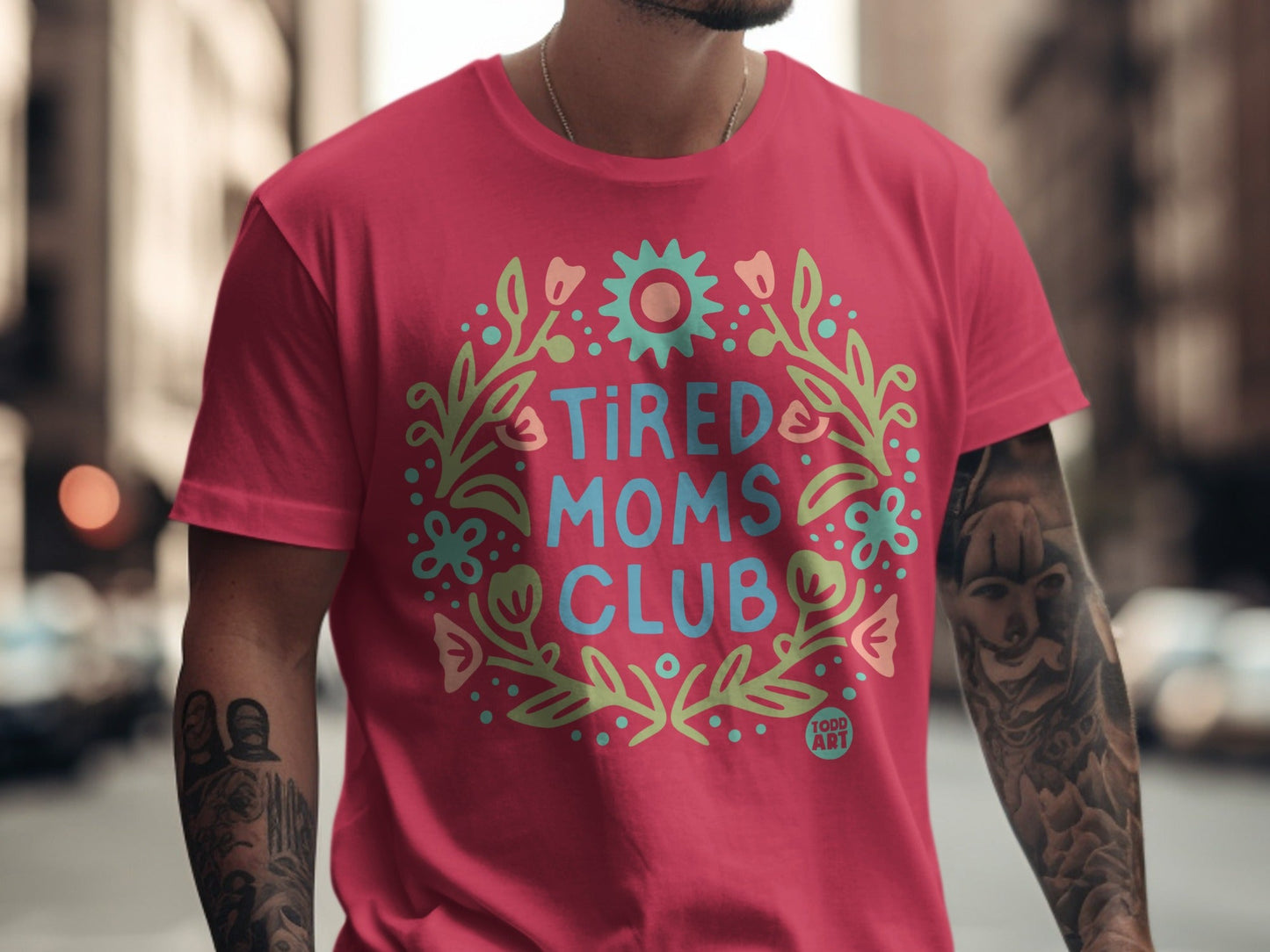 Pink t-shirt with "Tired Moms Club" in a floral wreath graphic.