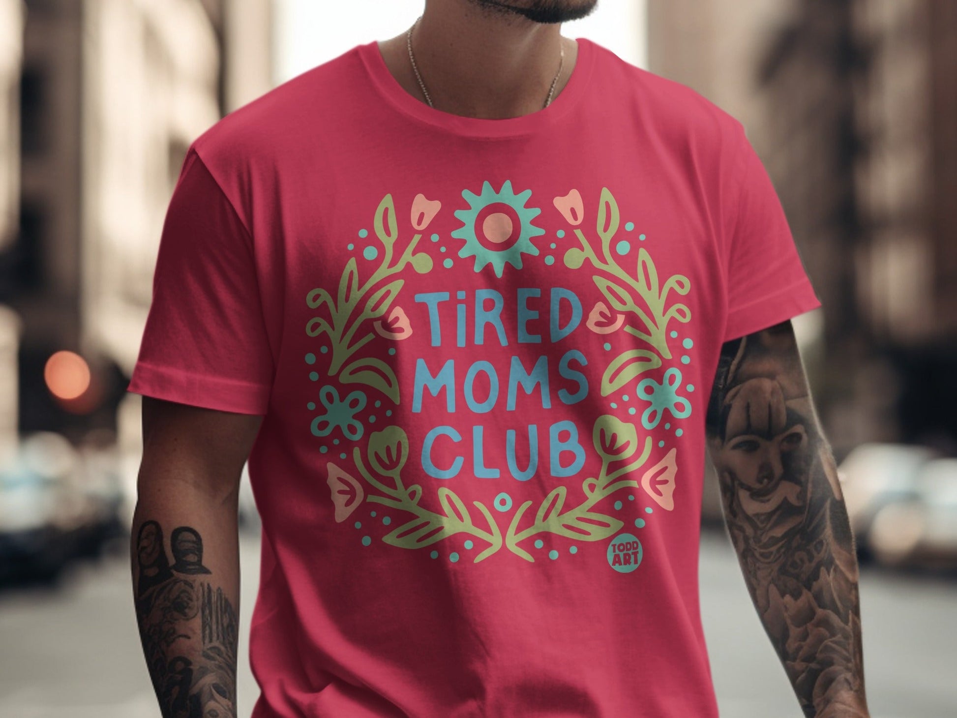 Pink t-shirt with "Tired Moms Club" in a floral wreath graphic.