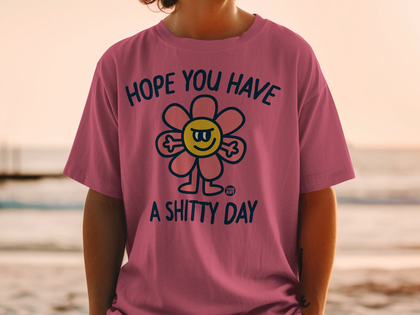 Pink t-shirt with a cartoon flower graphic and text "HOPE YOU HAVE A SHITTY DAY".