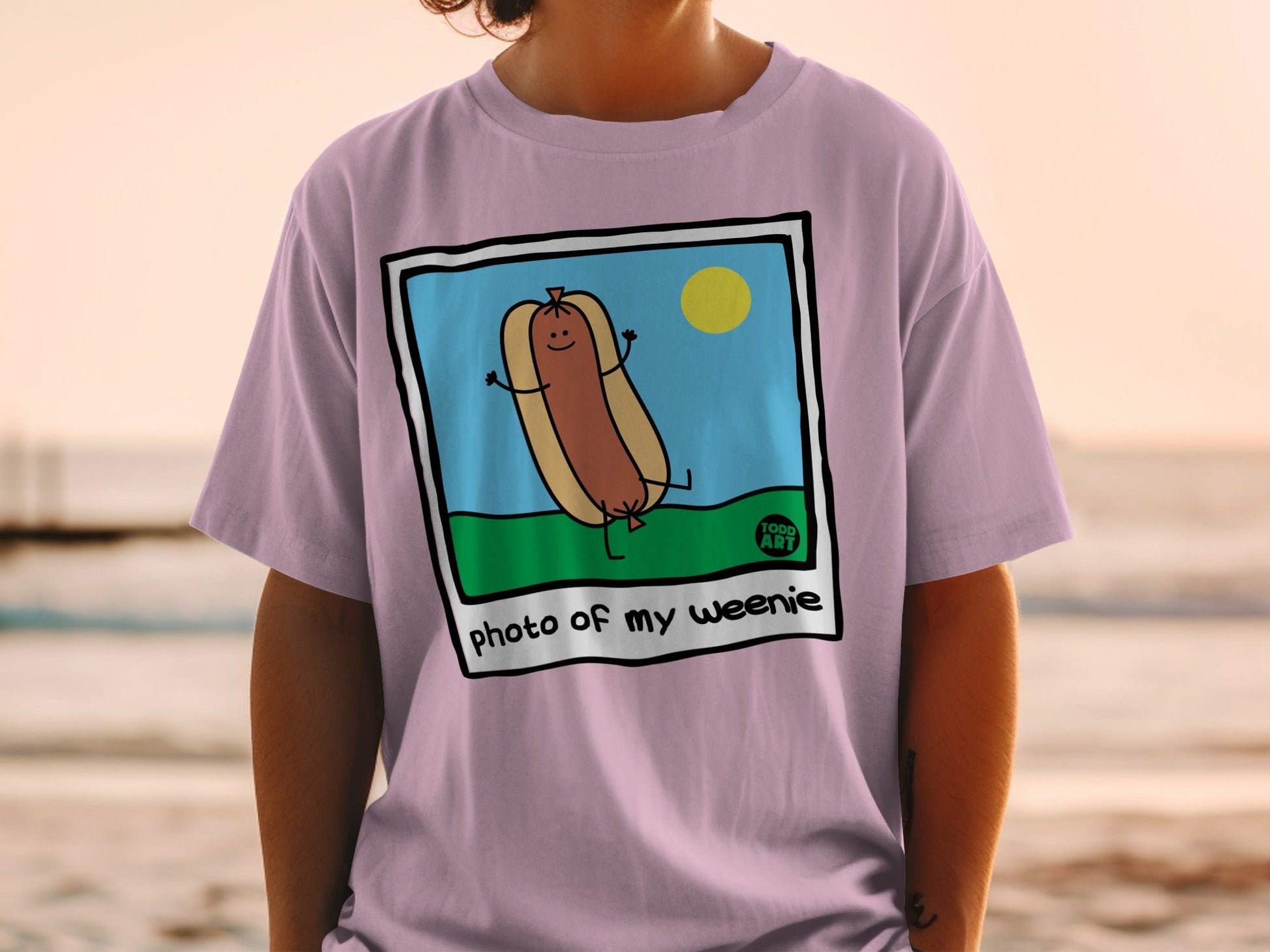 Illustration of a happy hot dog with text "photo of my weenie" on a purple t-shirt.