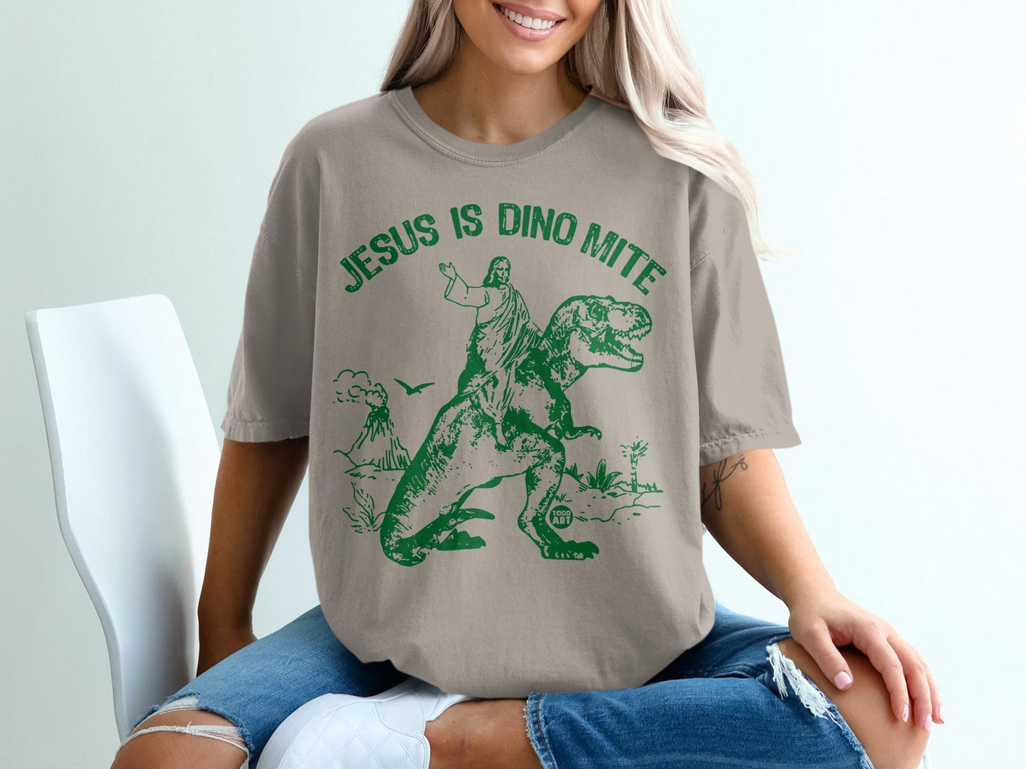 T-shirt with graphic of Jesus riding a dinosaur, "Jesus is Dino Mite" text.