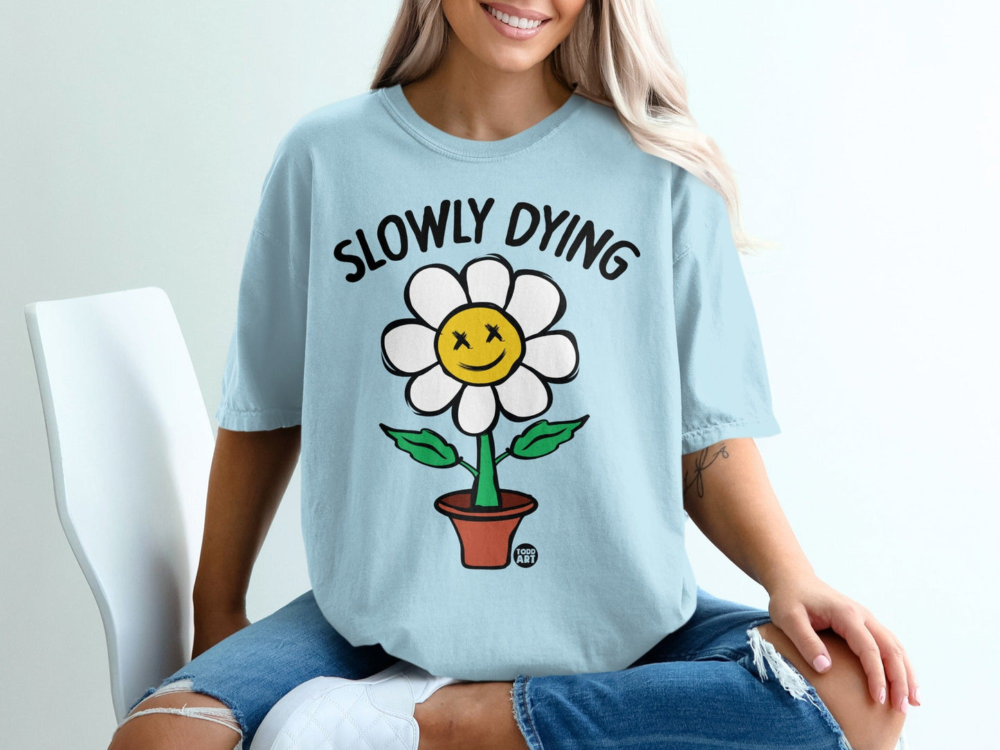 Light blue t-shirt with a cartoon flower that says "Slowly Dying".